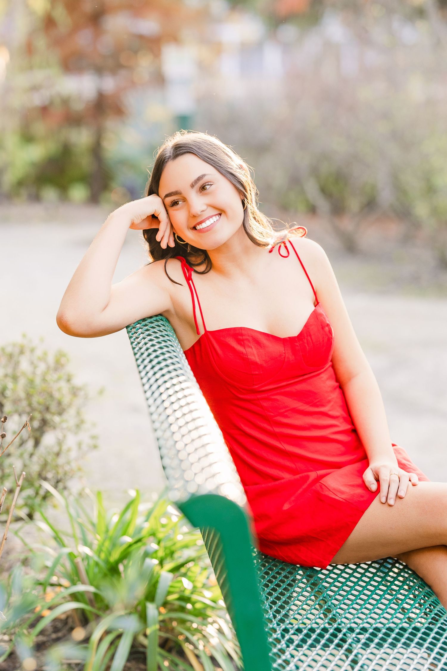A red sundress photoshoot in a garden setting with green bench and natural lighting.