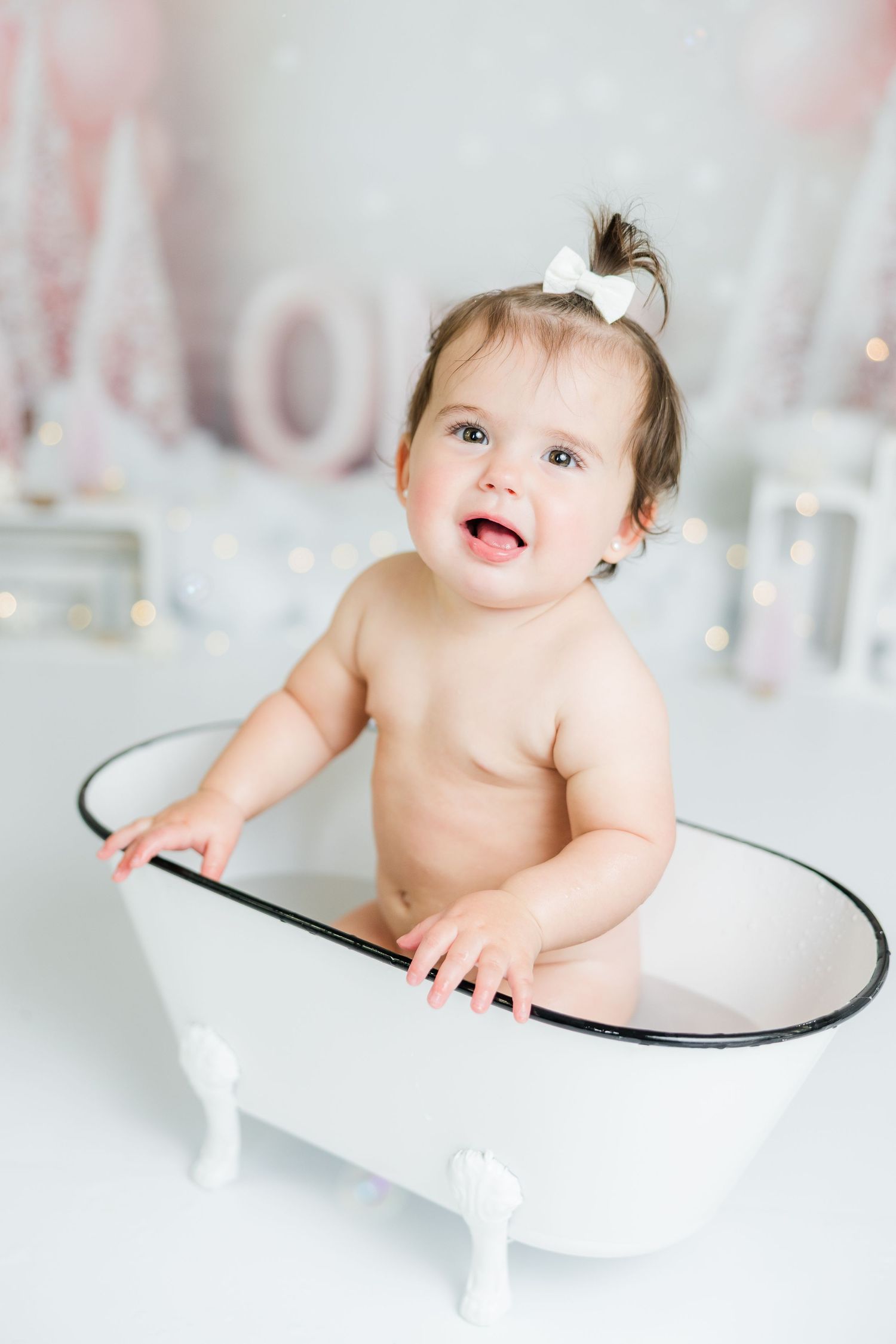 Baby sitting in white miniature bathtub during studio photo session.