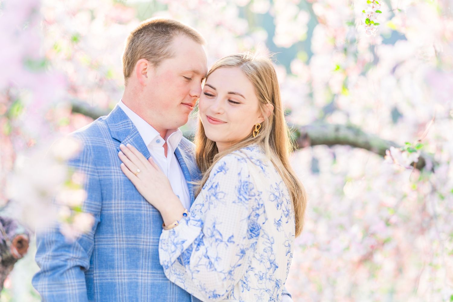 A romantic couple embraces among blooming spring cherry blossoms in soft pastel pink and blue tones.