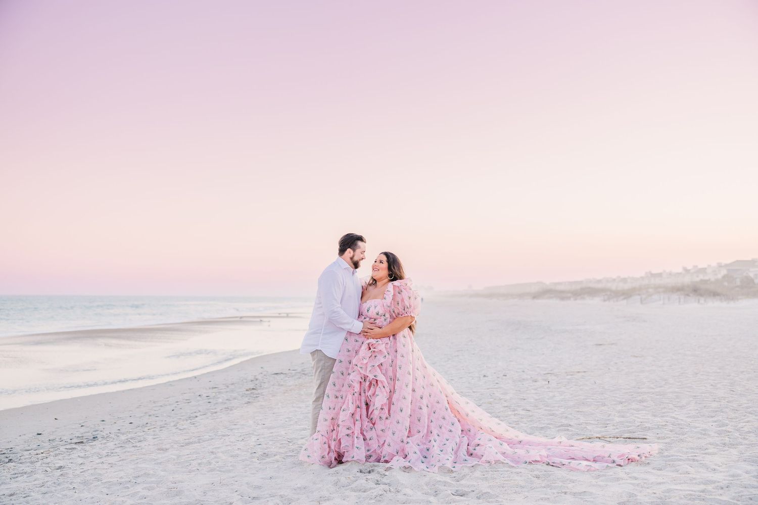 Romantic beach photoshoot with soft pink sunset and white sand dunes.