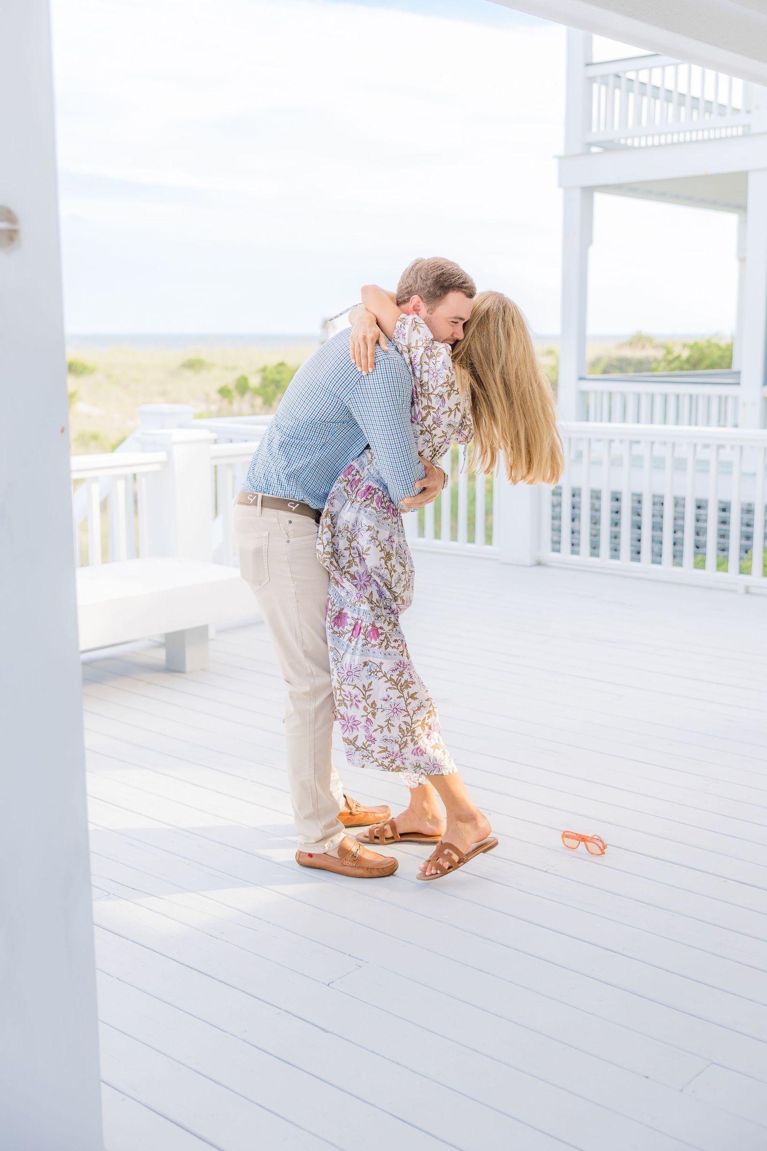 Couple in casual summer clothes sharing an intimate dance on a white coastal deck.