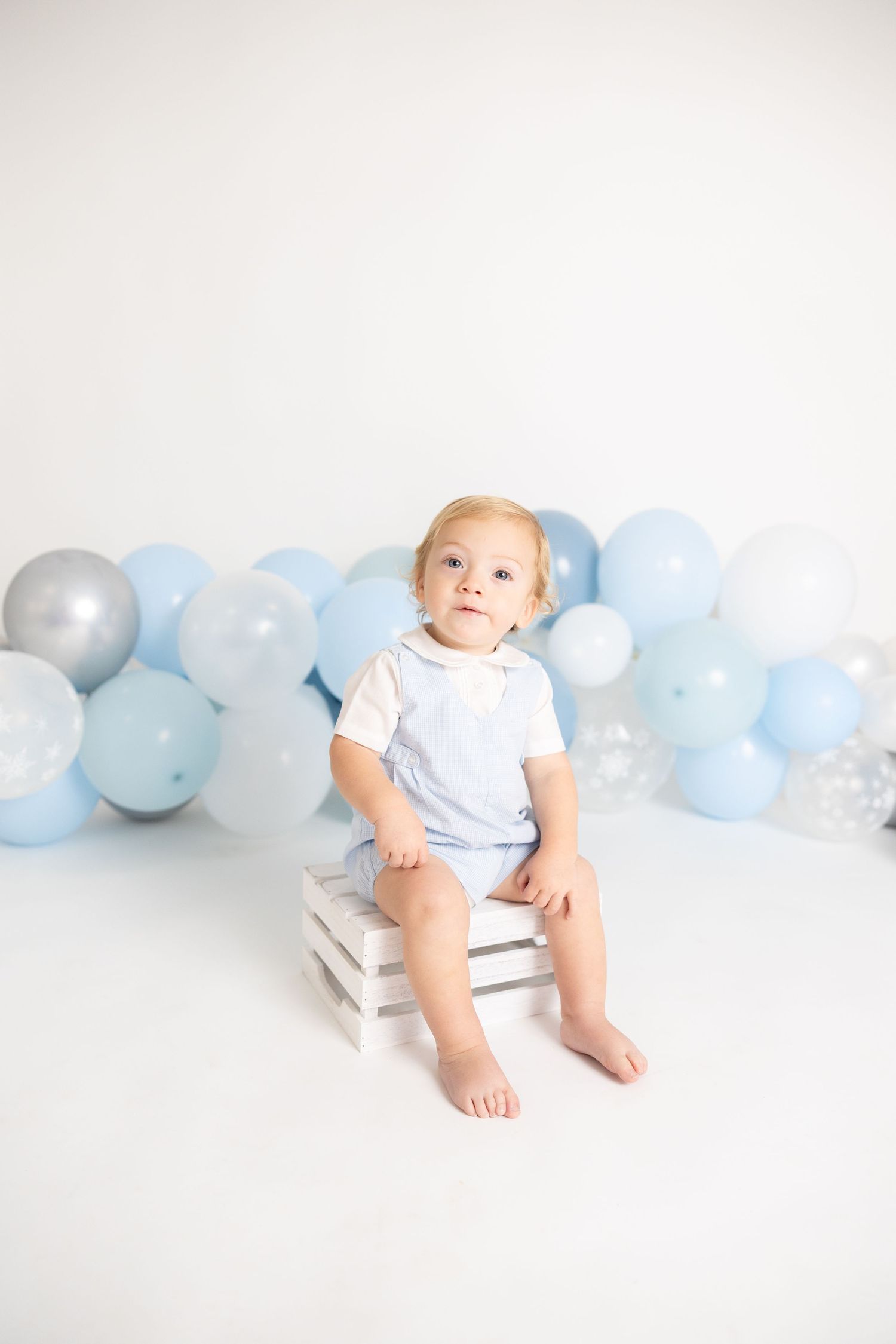 Baby sitting on stack of white books with blue balloon garland in background.