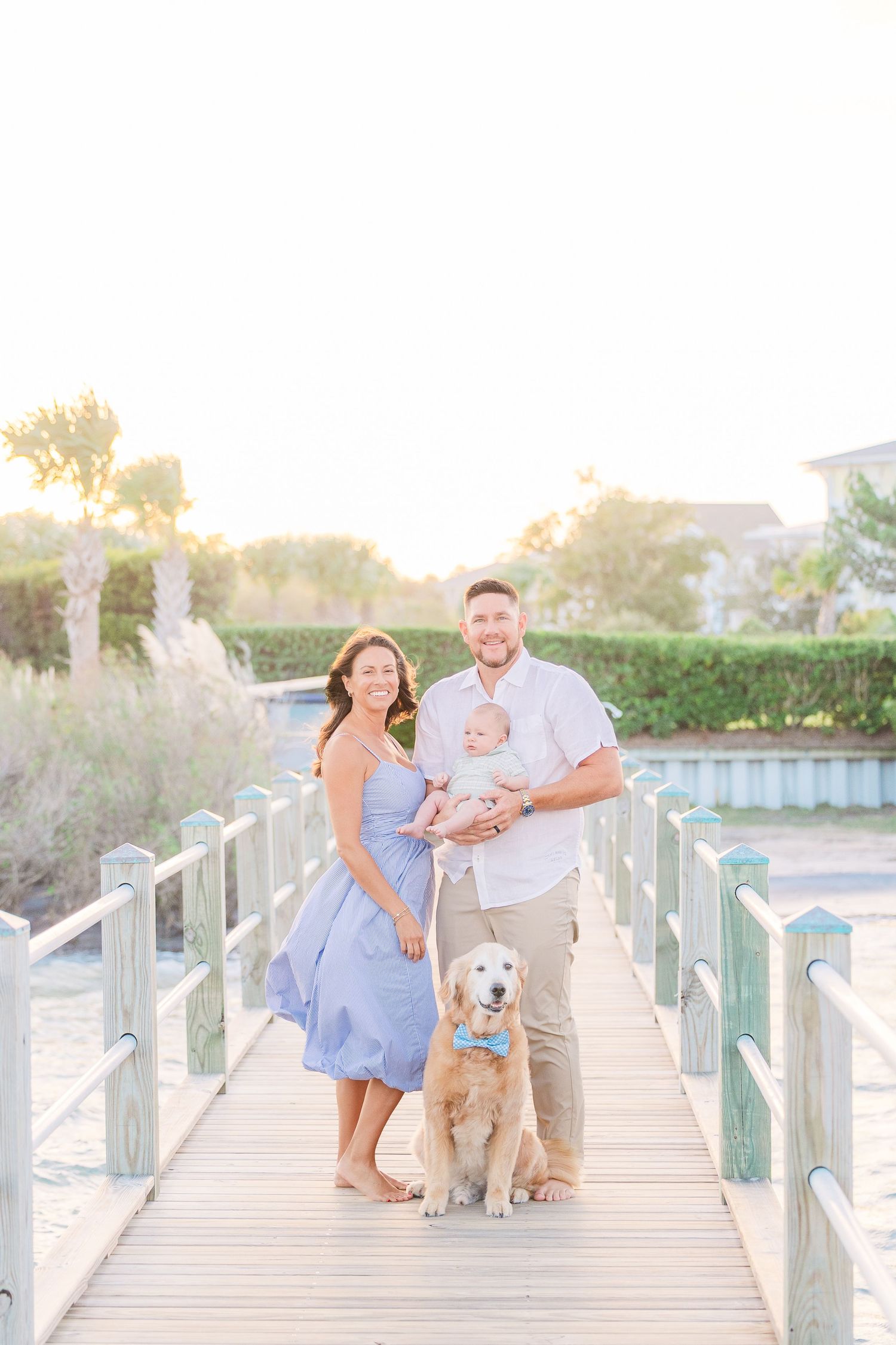 Family and golden retriever walk along coastal boardwalk during sunset photoshoot.