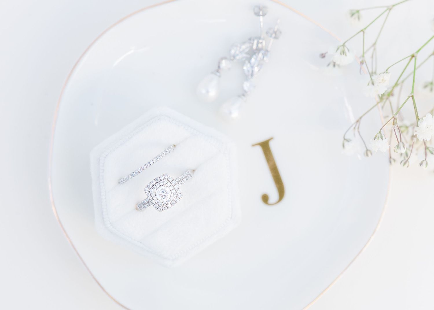 Diamond engagement ring in white velvet hexagon box on monogram J plate with pearl bracelet and baby's breath flowers in Airlie Gardens in W