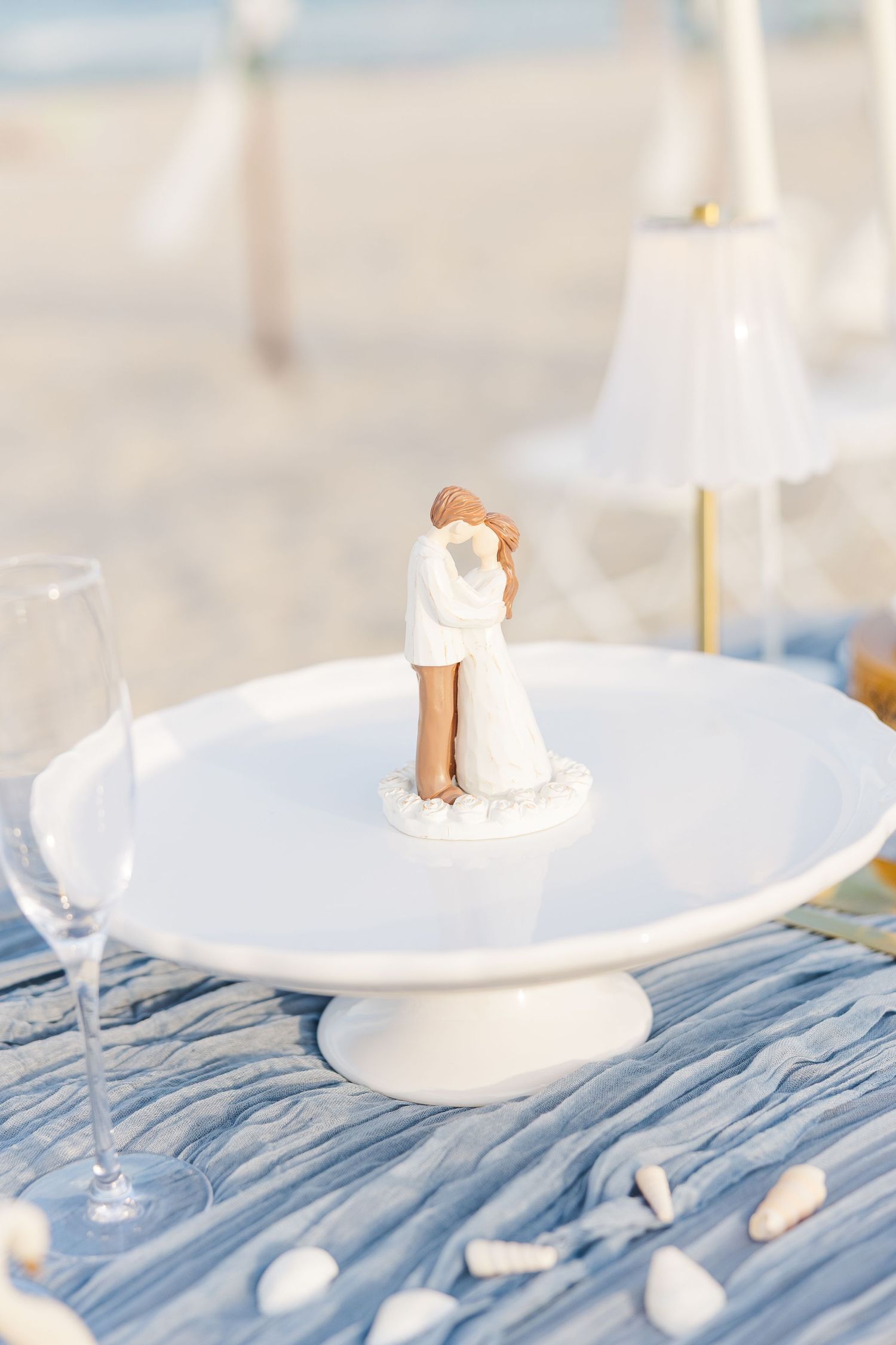 Wedding cake topper figurine of kissing couple displayed on white pedestal at beach reception in Carolina Beach near Wilmington, NC.