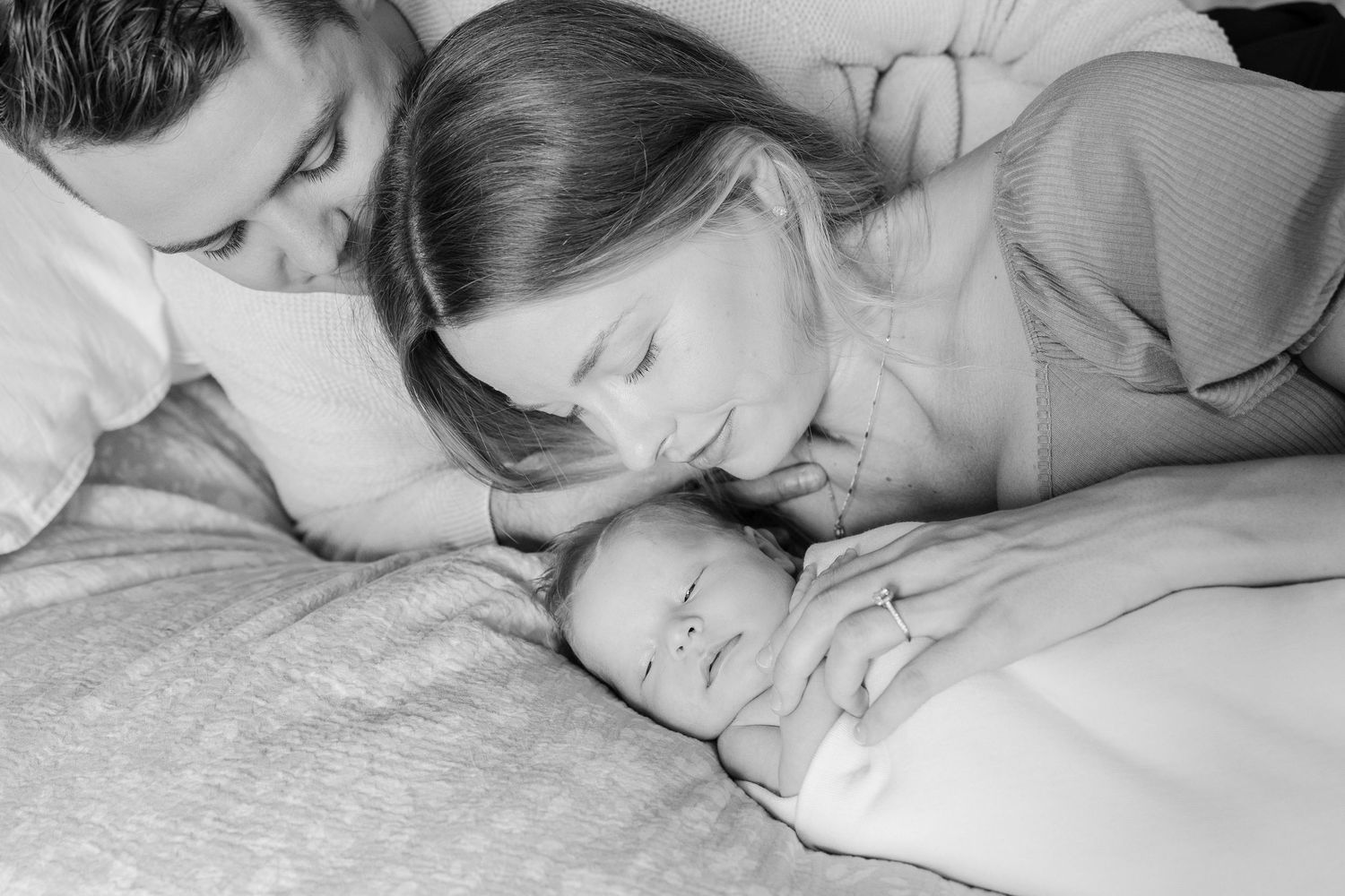 Black and white image of family cuddling together on bed during newborn session.