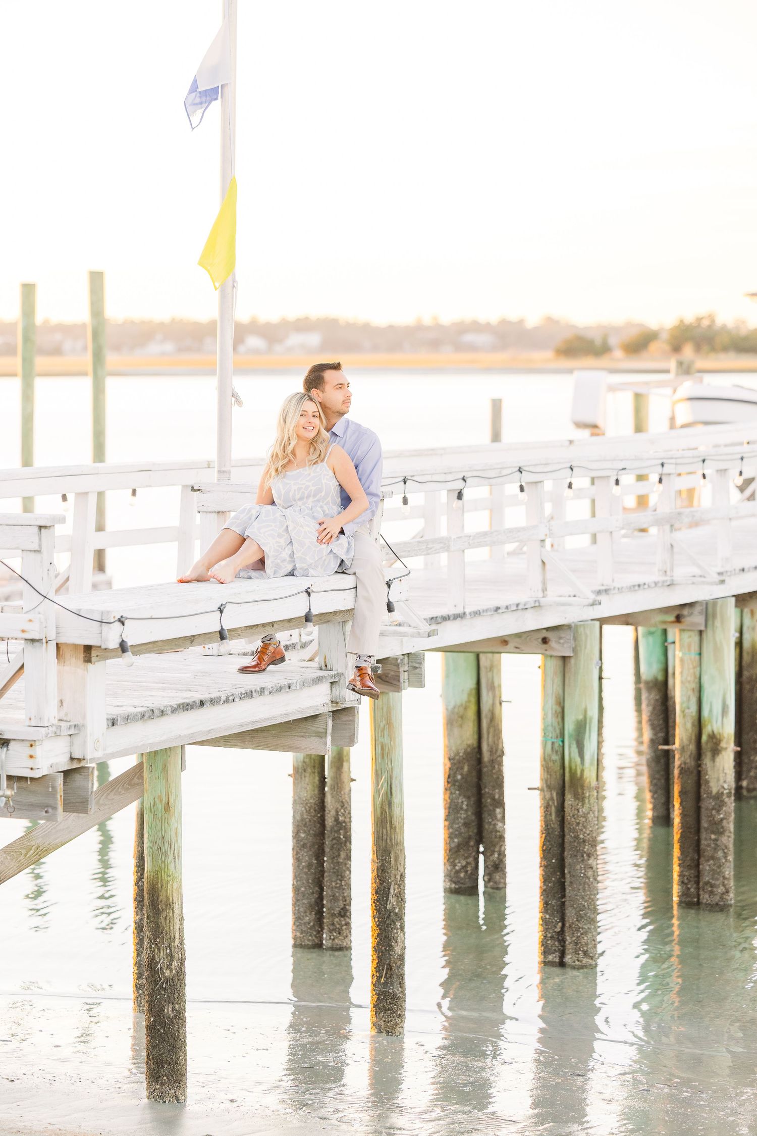 Couple sitting on white dock overlooking water during golden hour with nautical elements.
