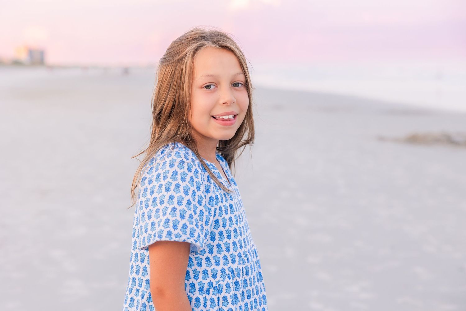 Girl in blue patterned dress enjoying a sunset beach photoshoot.