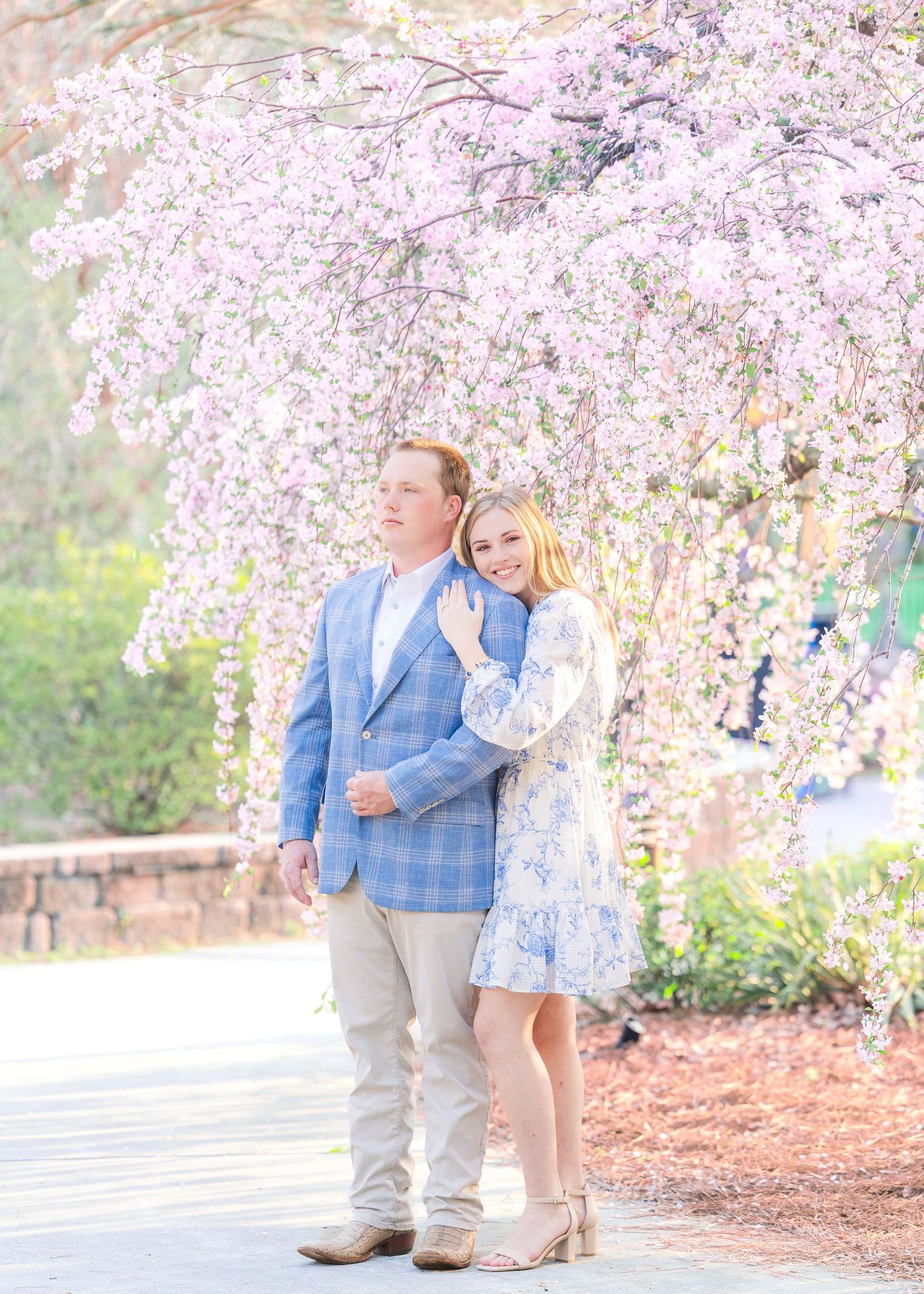A couple shares a tender moment under blooming cherry blossom trees in a springtime garden setting.