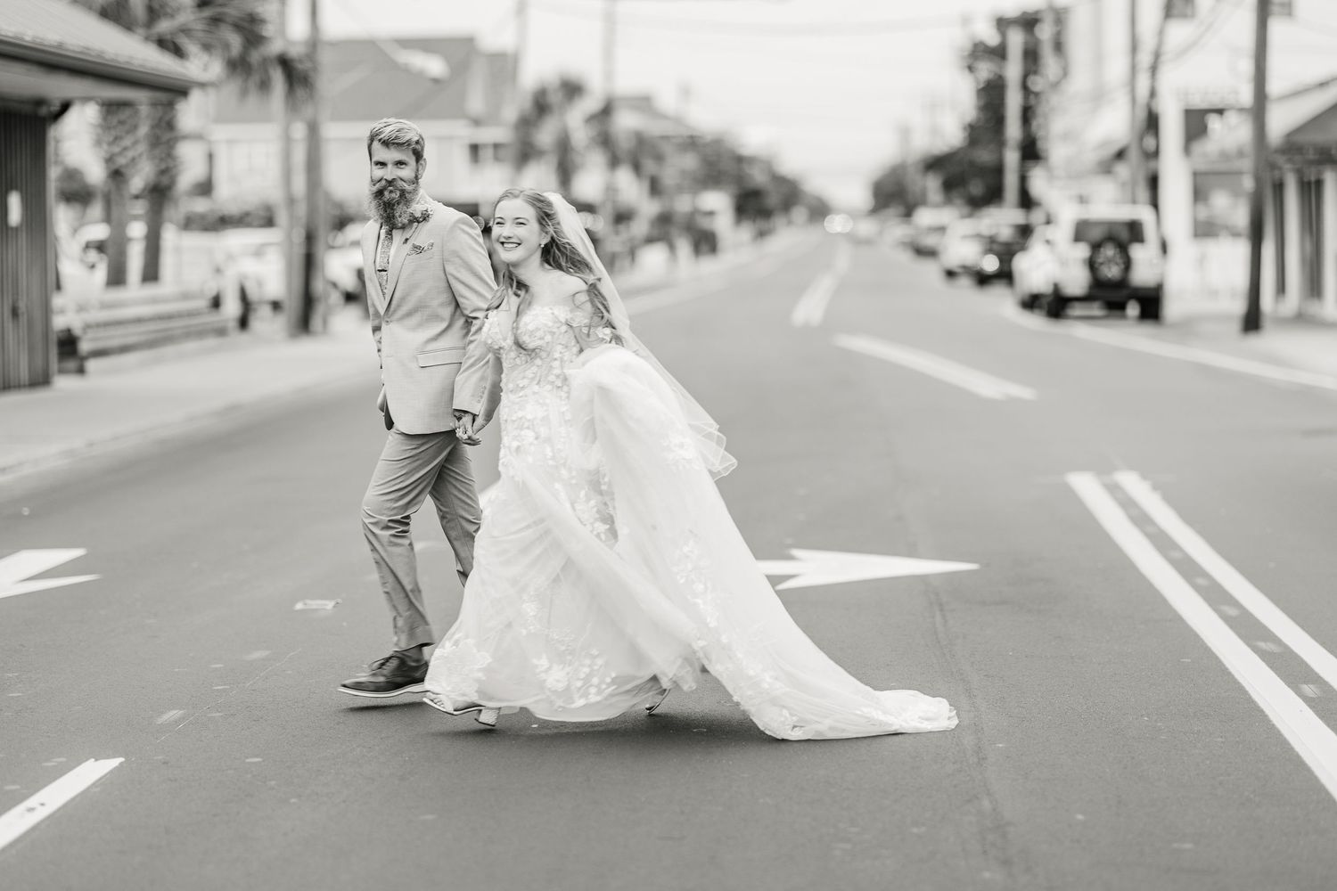 Black and white photo of newlyweds playfully posing on an empty street in Wrightsville Beach, nc after their wedding in wilmington