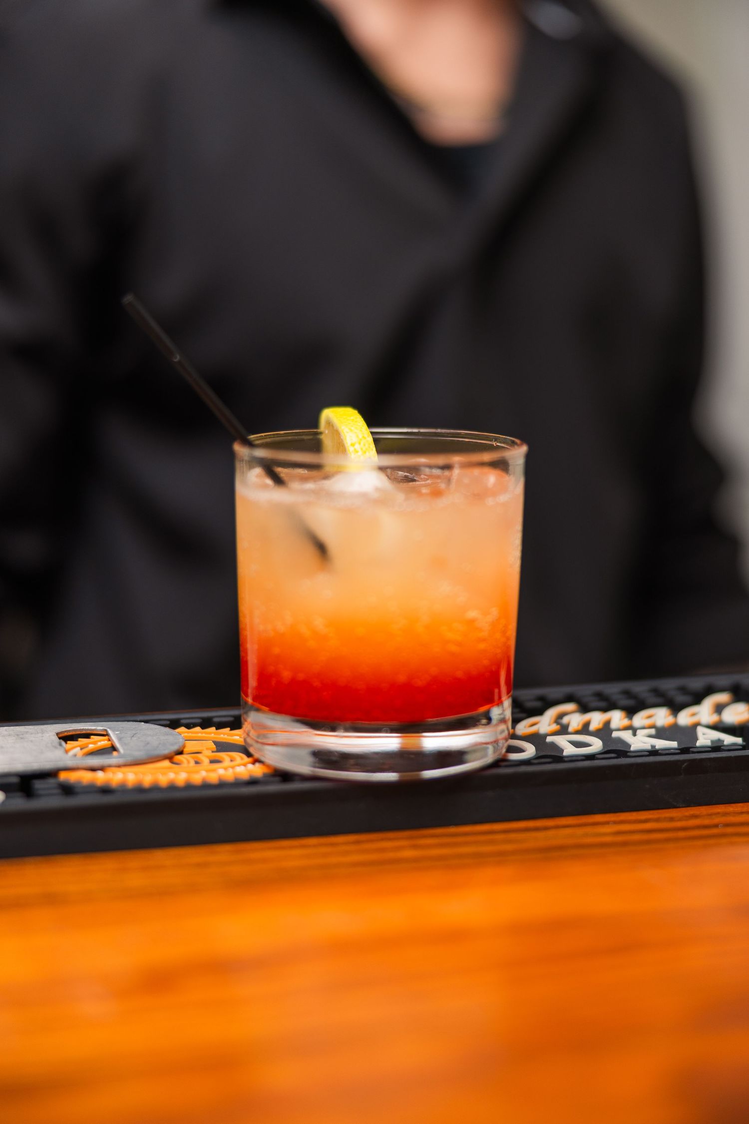 Orange cocktails with lemon garnish lined up on a wooden bar counter.