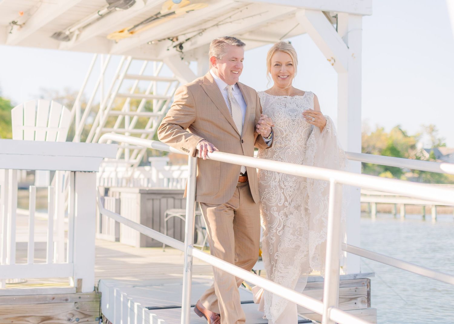 A couple embraces on a white wooden porch overlooking the water.