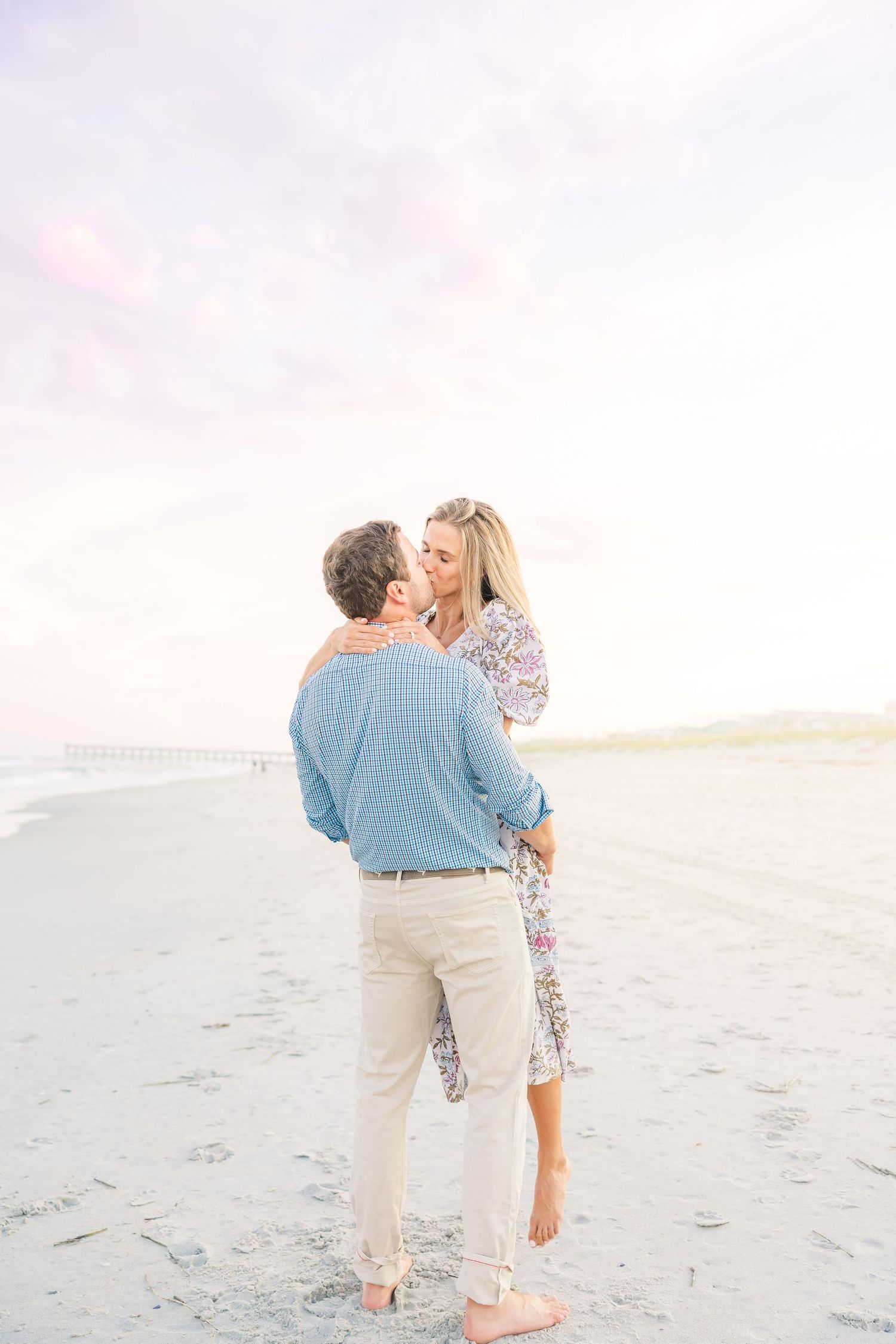 Playful moment between couple on beach with soft pastel sky.