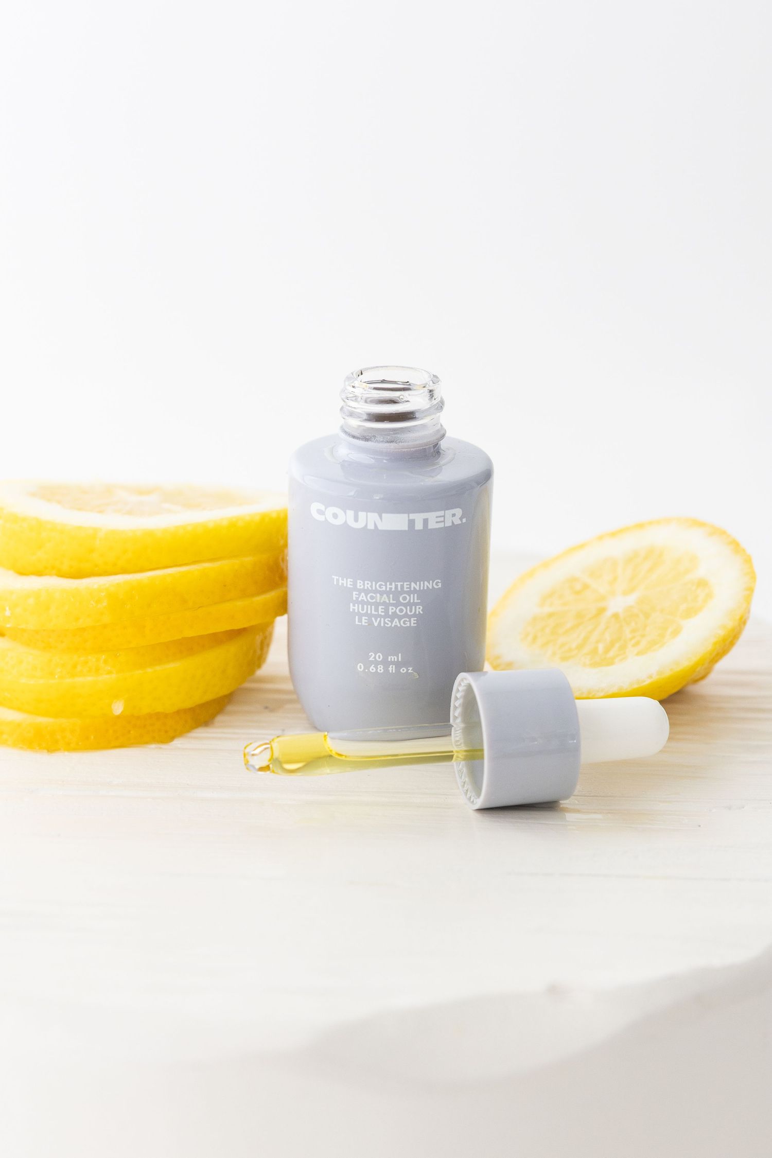 Grey dropper bottle with fresh lemon slices on white surface.