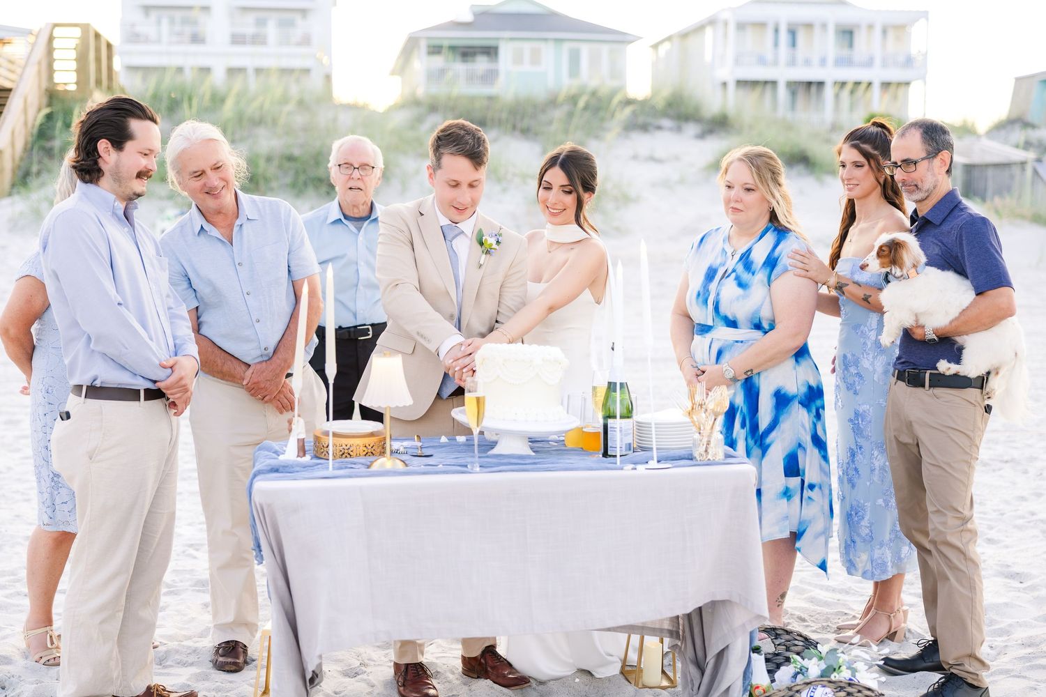 Bride and groom cut wedding cake at outdoor beach reception surrounded by smiling family and guests in Carolina Beach near Wilmington, NC.