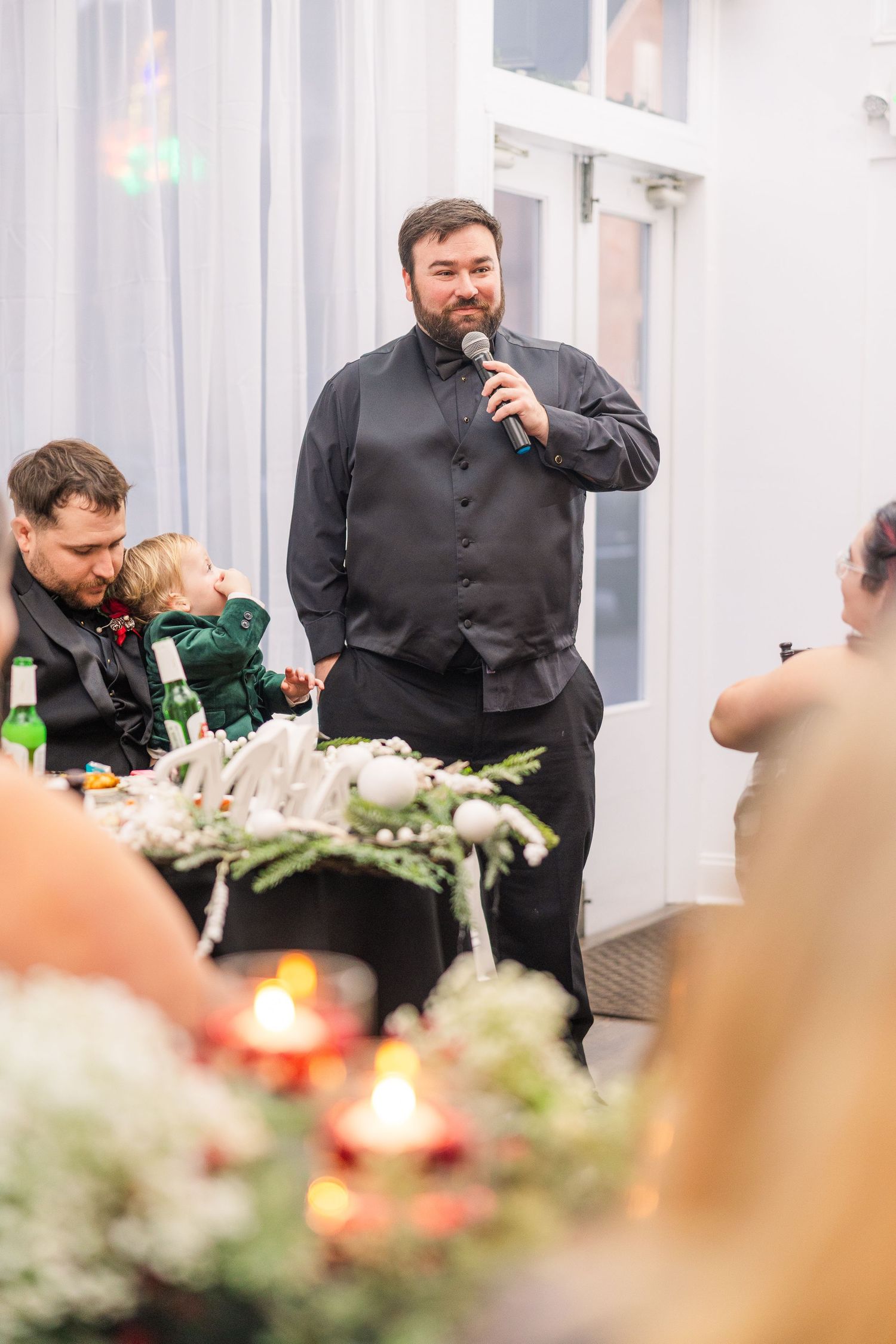 Wedding reception dinner with table decorations and greenery in white interior space.
