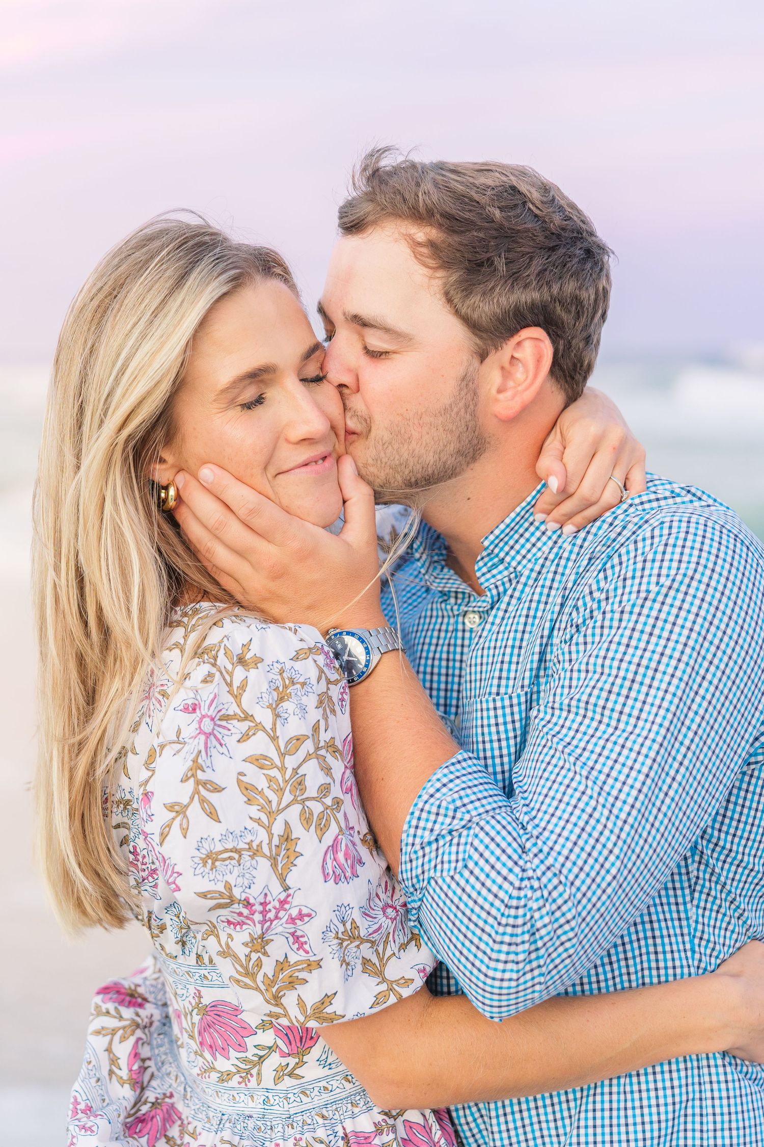 Tender moment between couple on beach with soft sunset lighting.