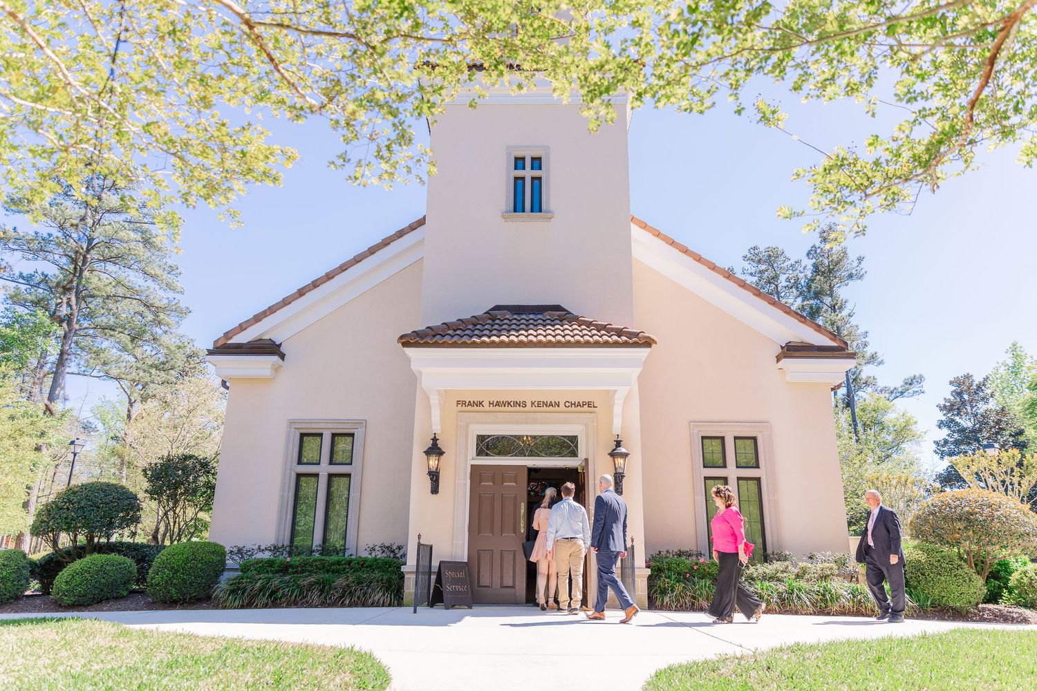 People gather outside a beautiful Mediterranean-style church with white stucco walls.
