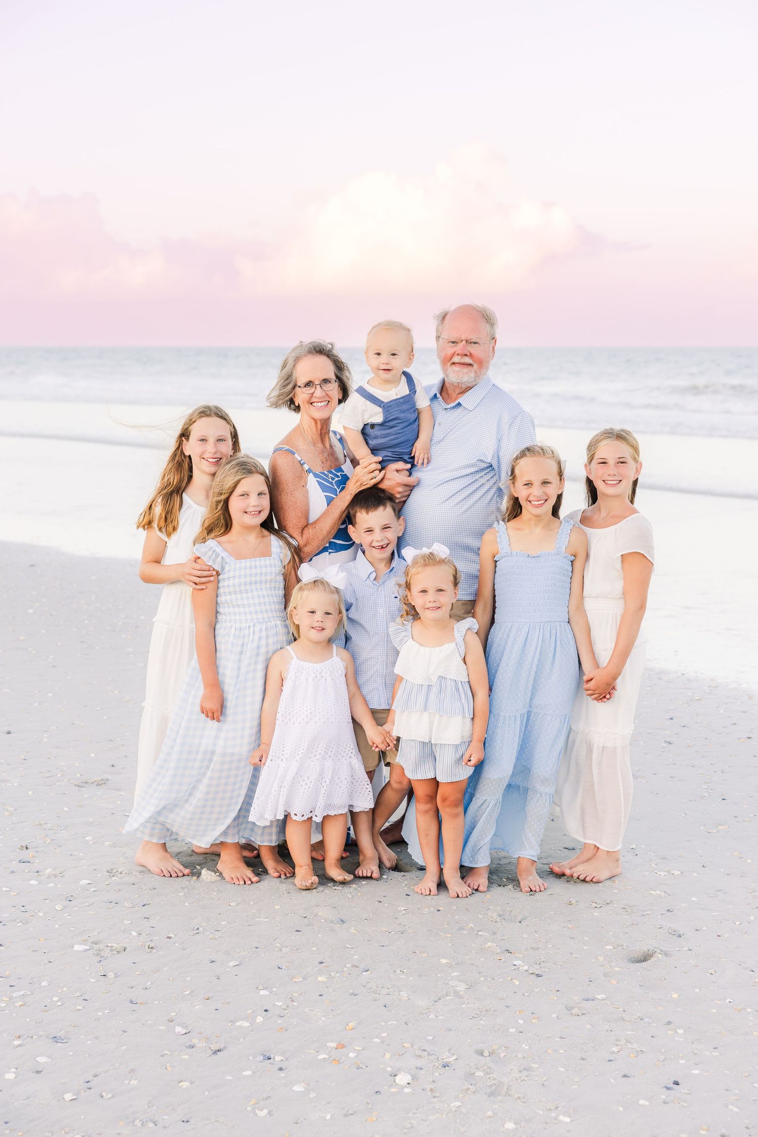 Extended family portrait on beach wearing coordinated blue and white outfits at sunset.
