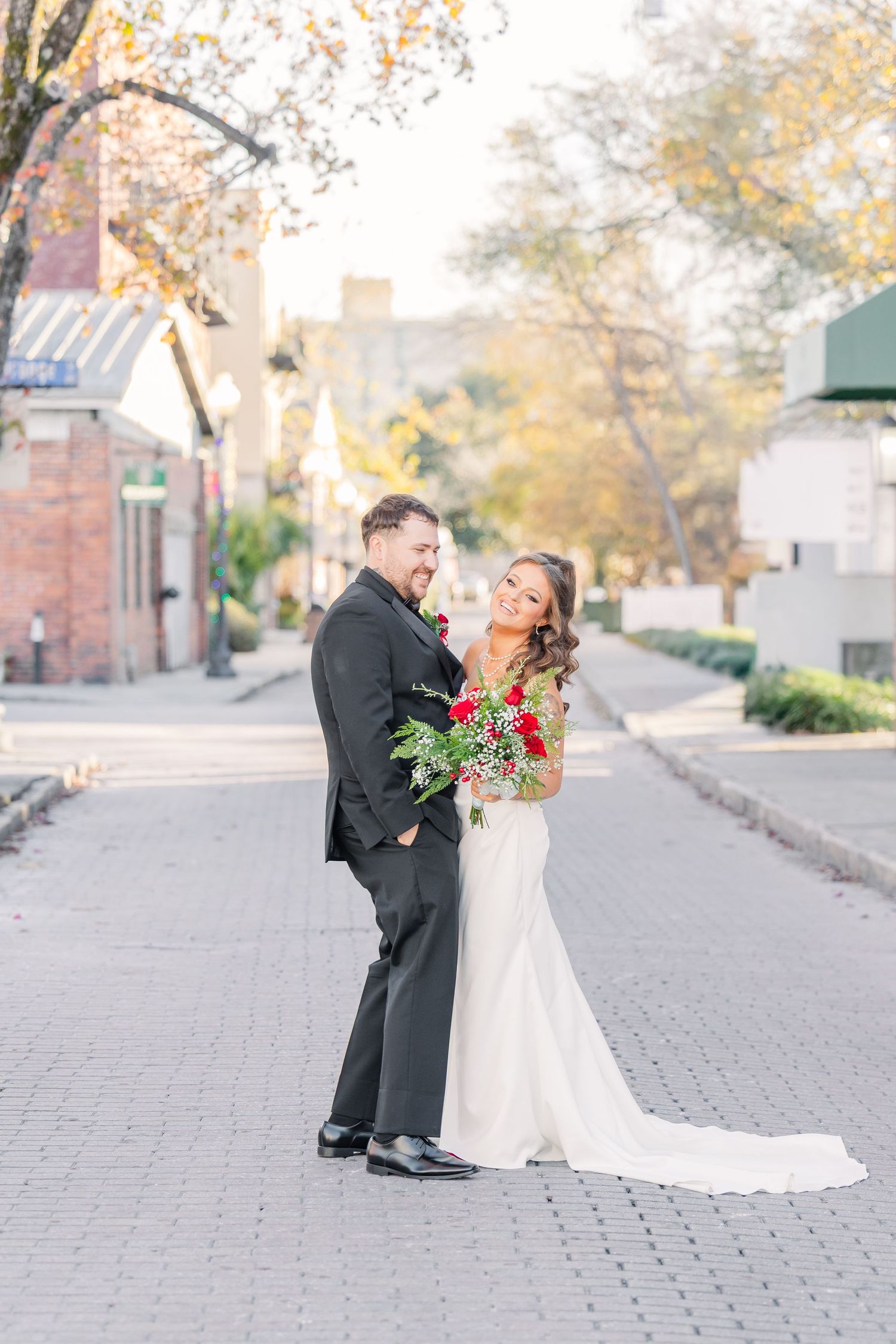 A wedding couple poses on a brick paved street during an autumn day.