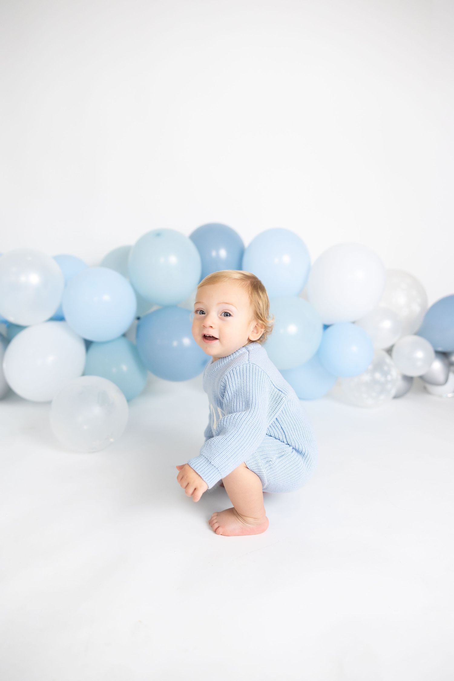 Baby crawling on white floor with blue and white balloon garland decoration.