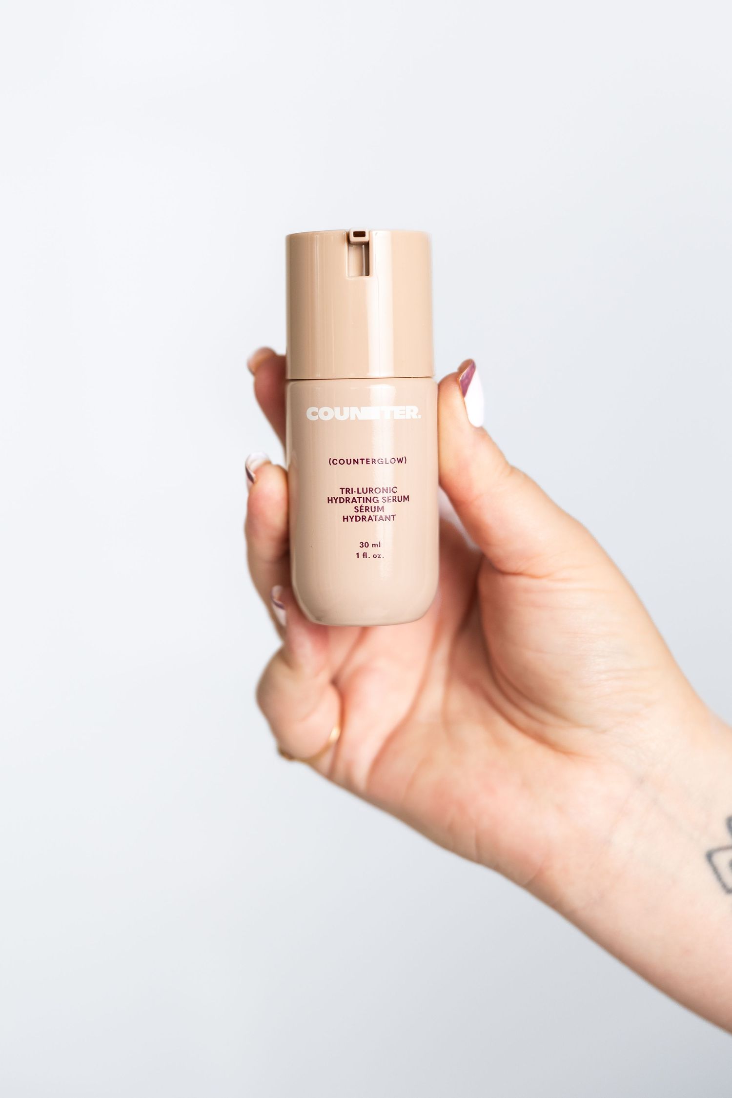 Hand holding a beige cosmetic container against white background.
