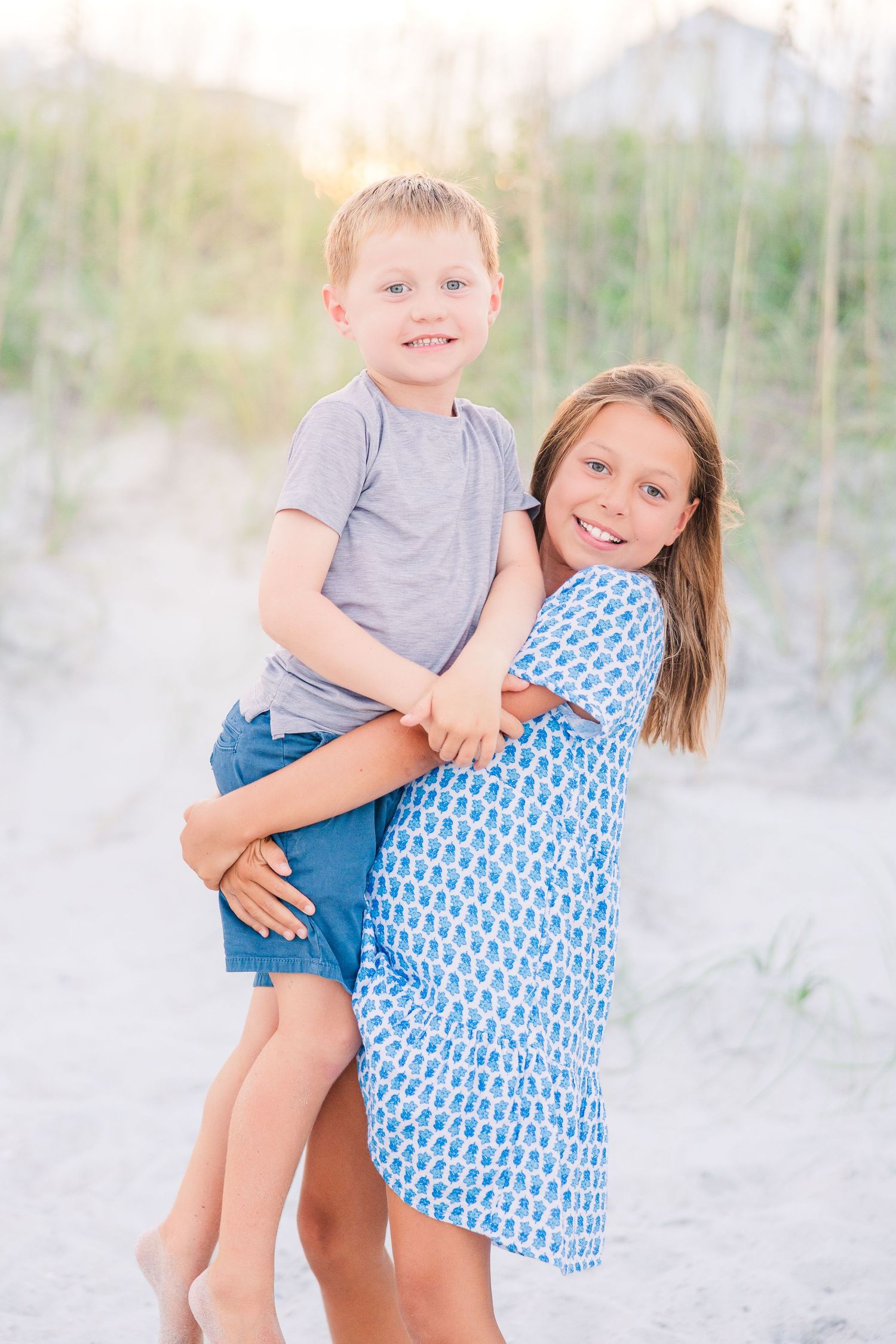 Two children posing playfully together on a sandy beach with soft lighting.