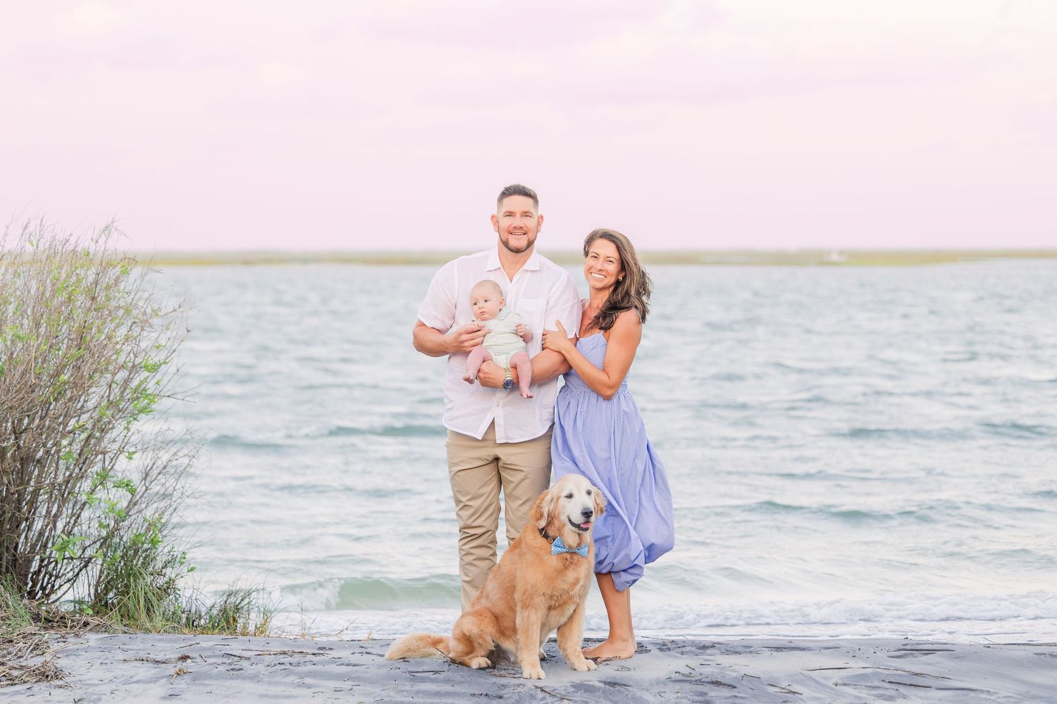 A couple and their dog enjoy a tender moment by the ocean at dusk.
