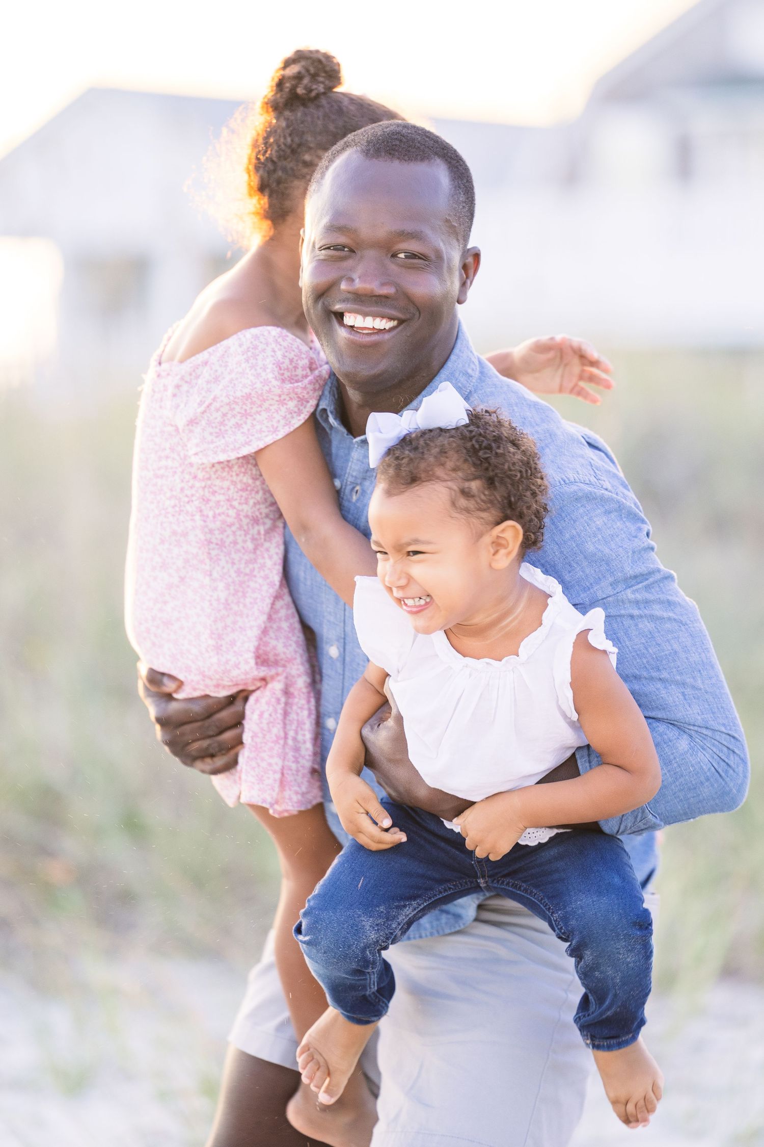 A heartwarming beach portrait of a parent holding two laughing children in casual attire.