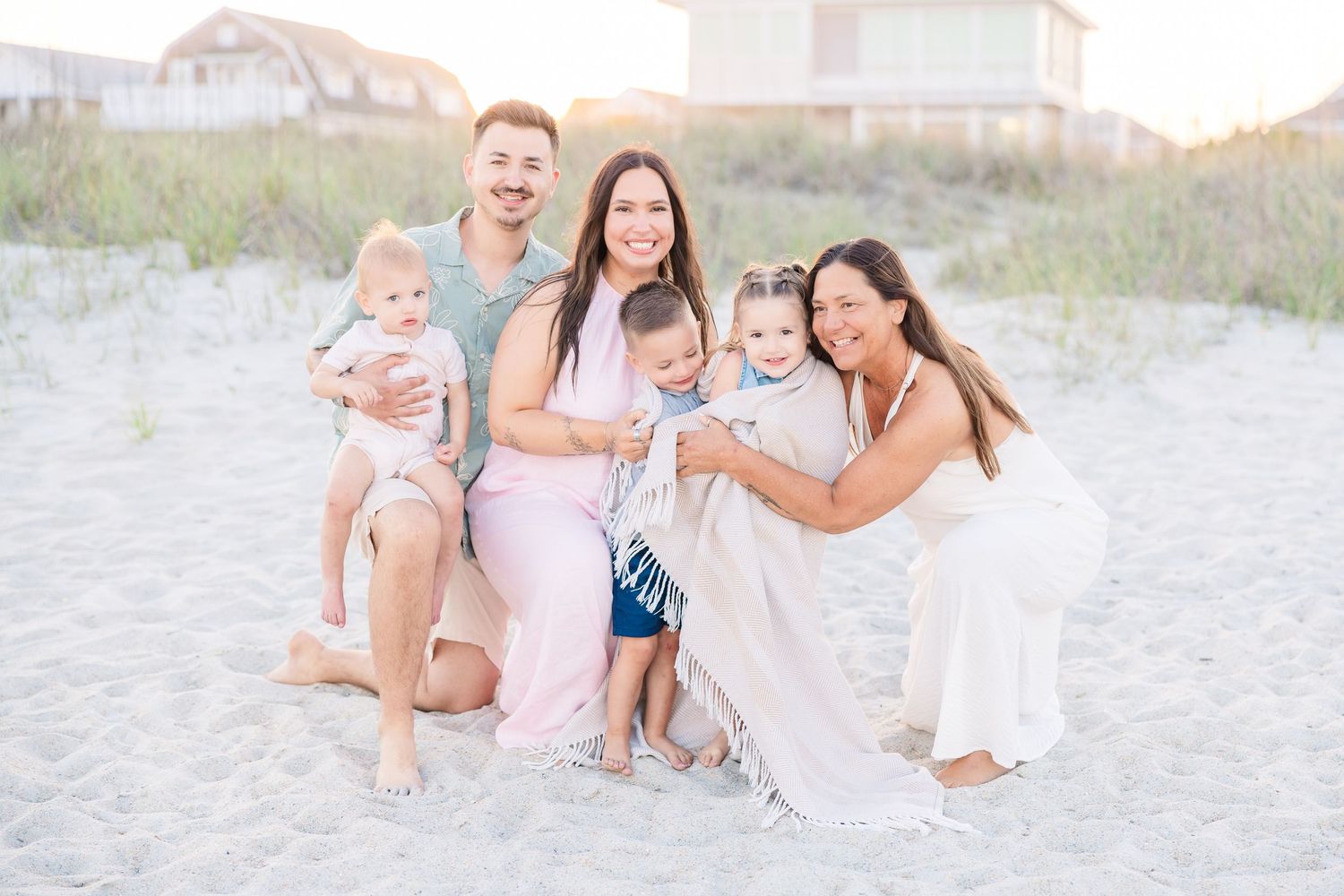 A family of six posing together on a sandy beach at golden hour sunset.