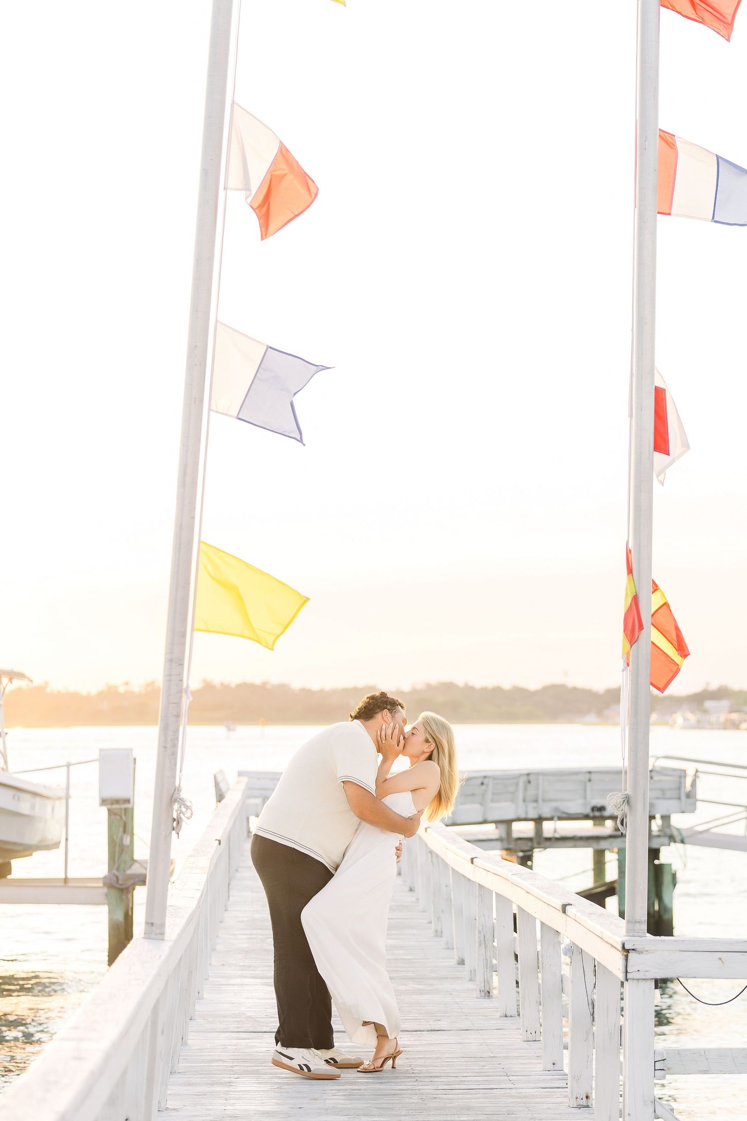 Couple shares a romantic dip kiss on a waterfront dock surrounded by colorful nautical flags.