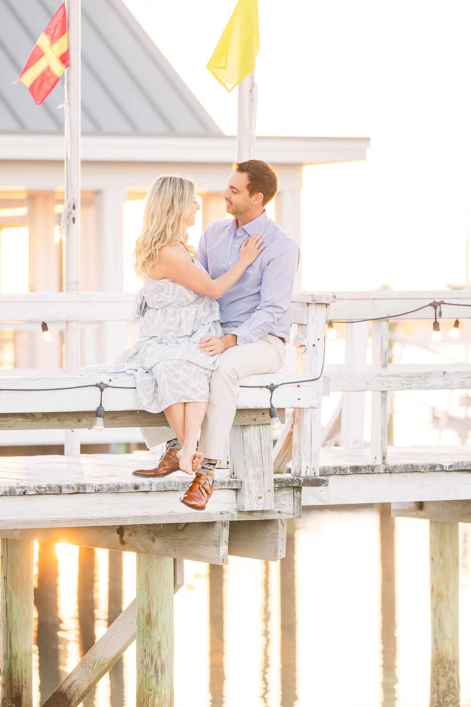 Couple shares romantic moment on wooden pier at sunset with flags waving in background.