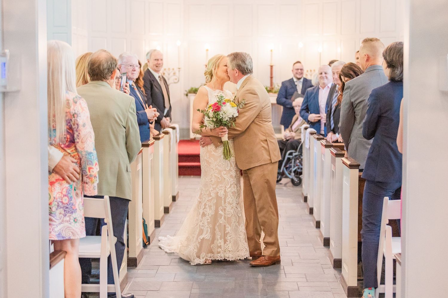 Church wedding scene showing rows of white pews filled with guests during a ceremony.