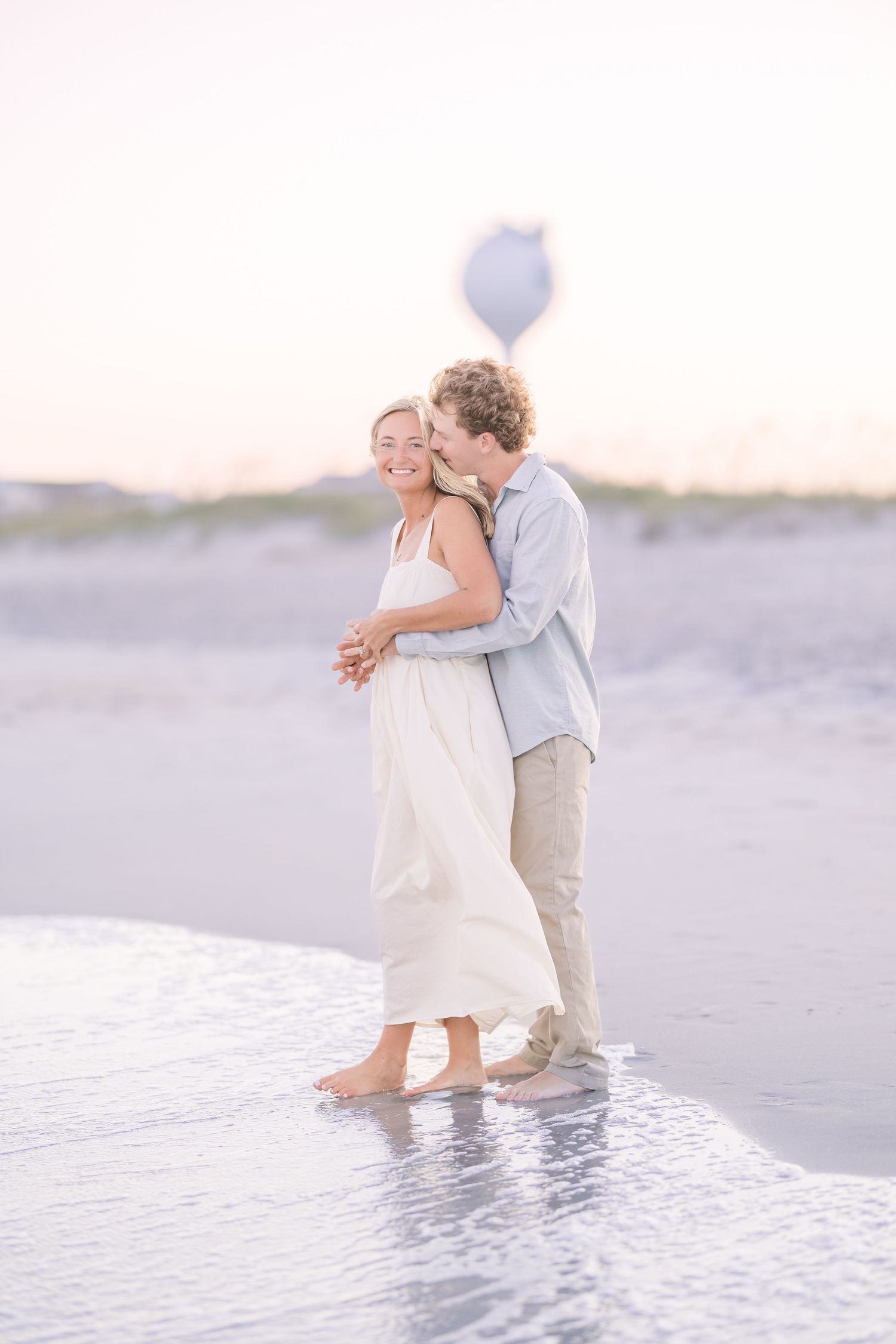 Couple wades through shallow ocean water during sunset photoshoot.