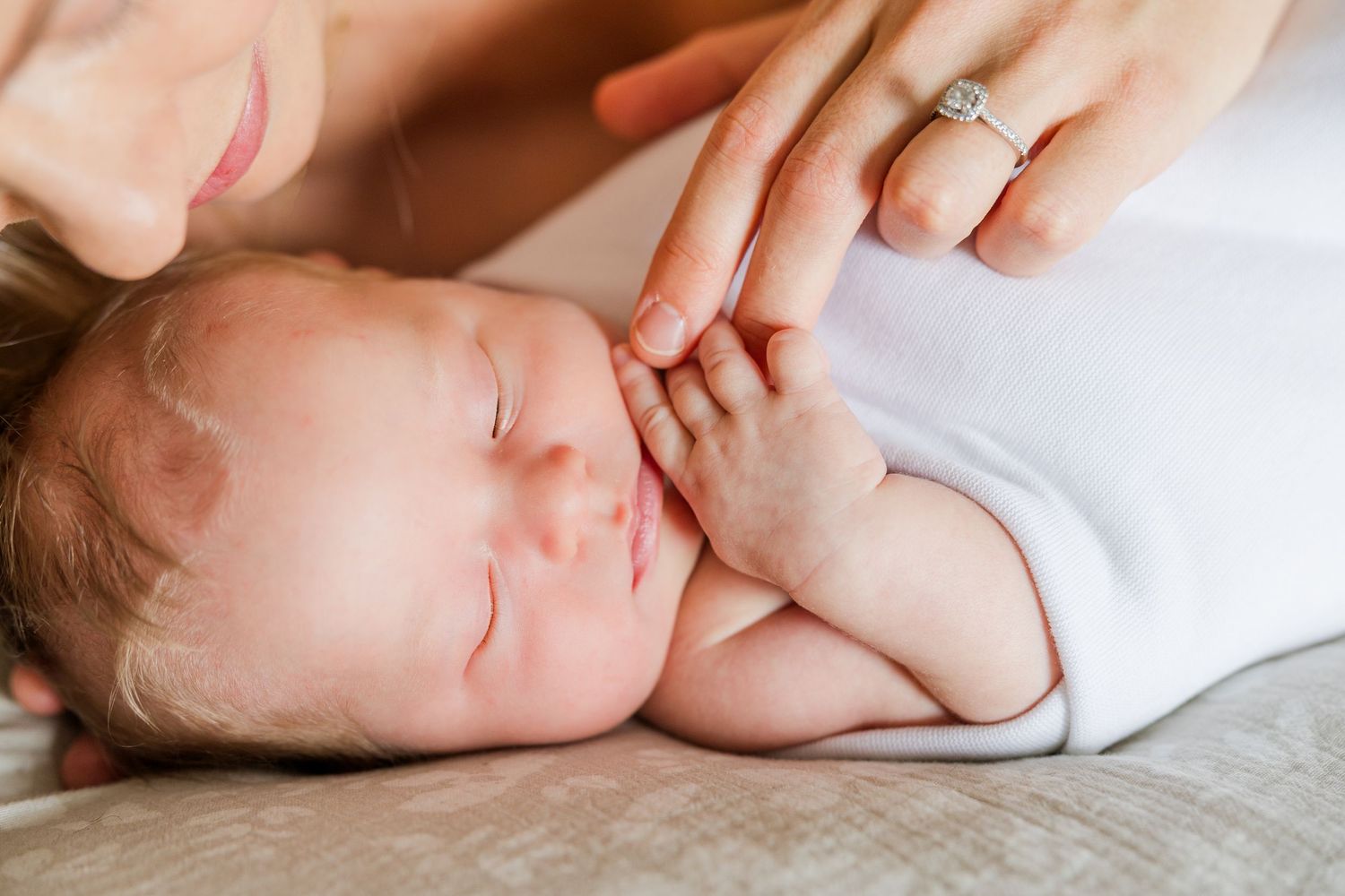 Newborn baby sleeping peacefully on white bedding with gentle lighting.