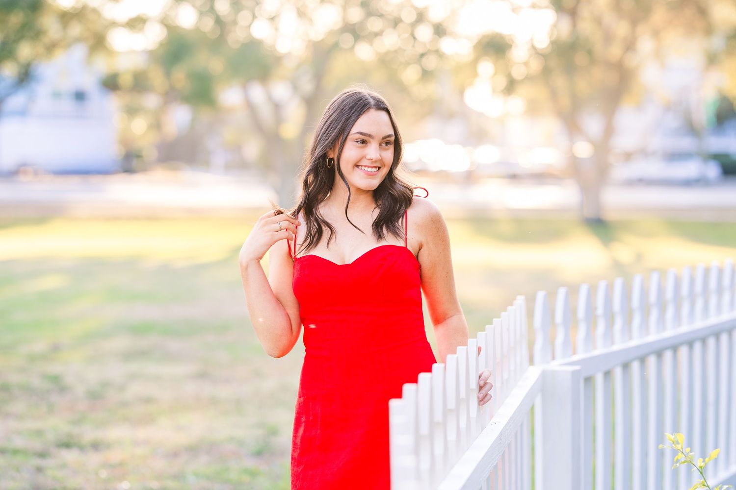 Red dress portrait by white picket fence during golden hour.