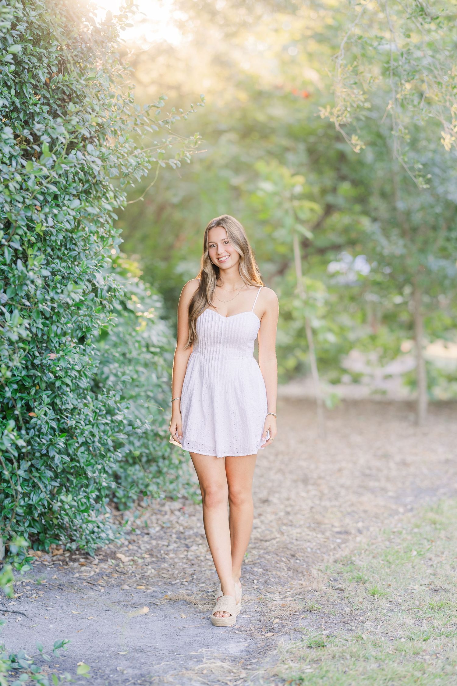 Figure in white sundress walks along a garden path during golden hour.