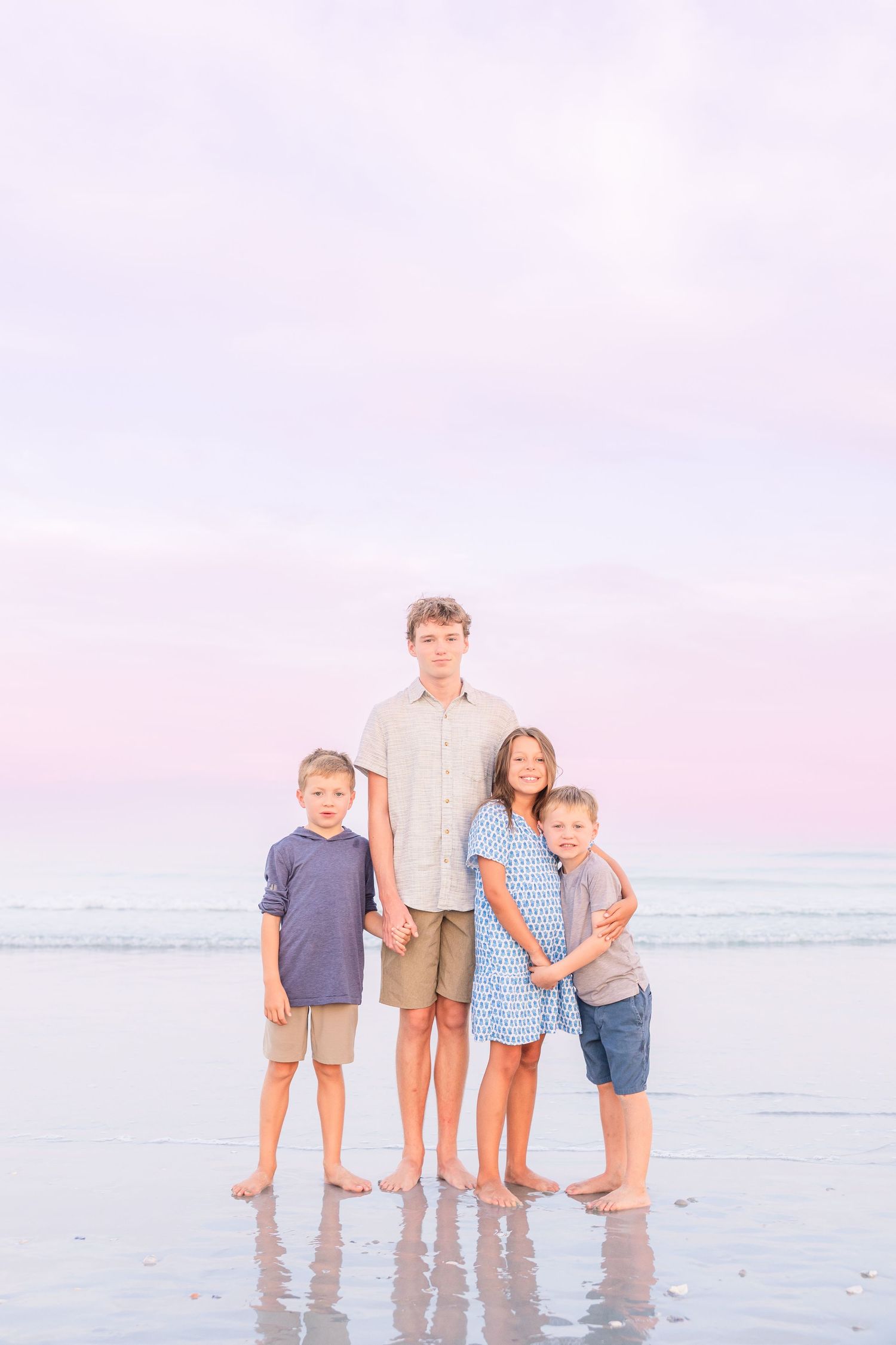 Family of four standing together in shallow ocean water during sunset photoshoot.