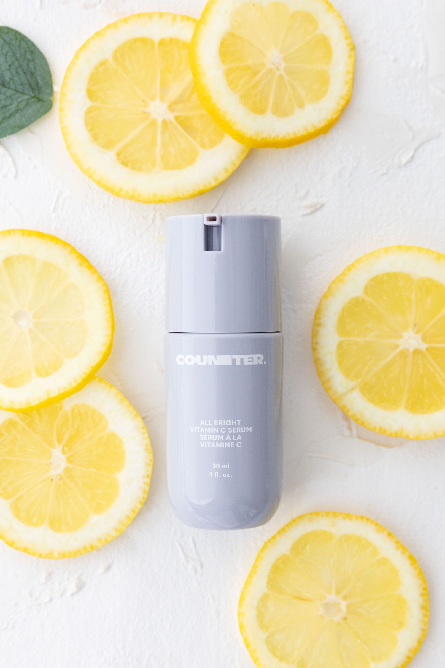 Skincare product bottle surrounded by fresh lemon slices on white surface.