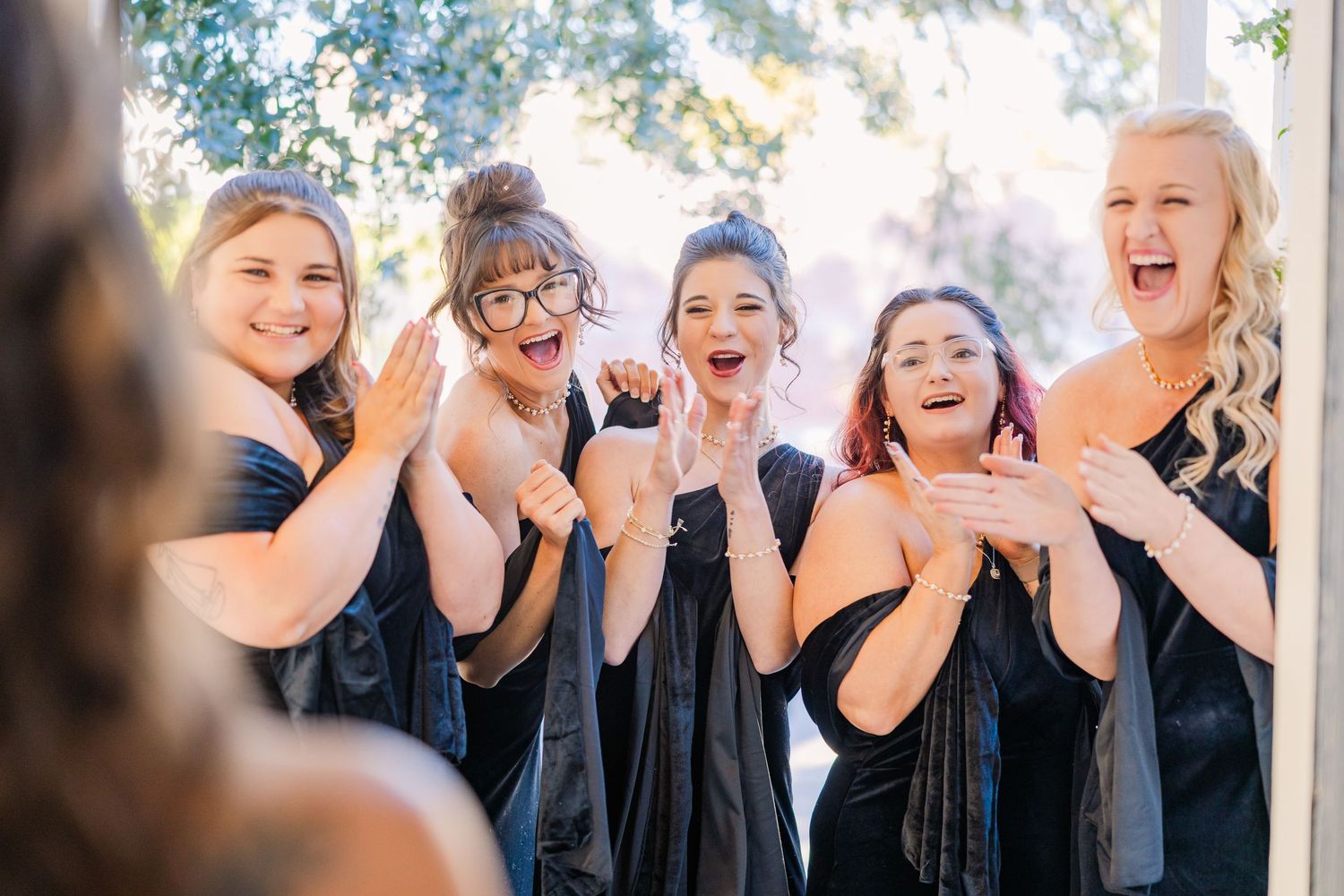 Bridesmaids in black dresses laugh and smile together during a wedding photoshoot.