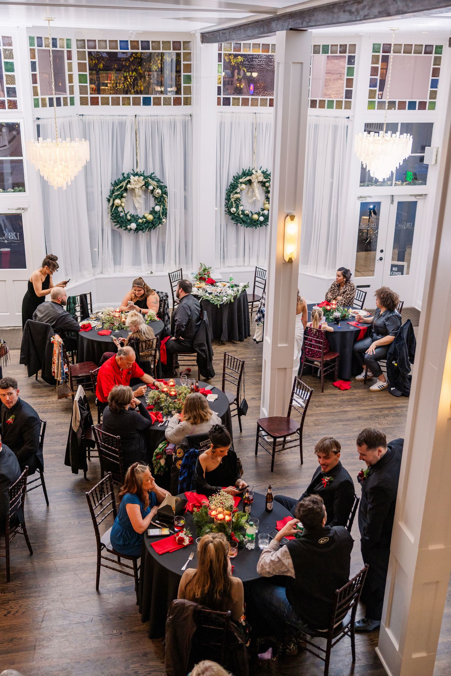 Elegant reception venue with white walls, holiday wreaths, and guests dining at round tables wedding groom bride wilmington North Carolina