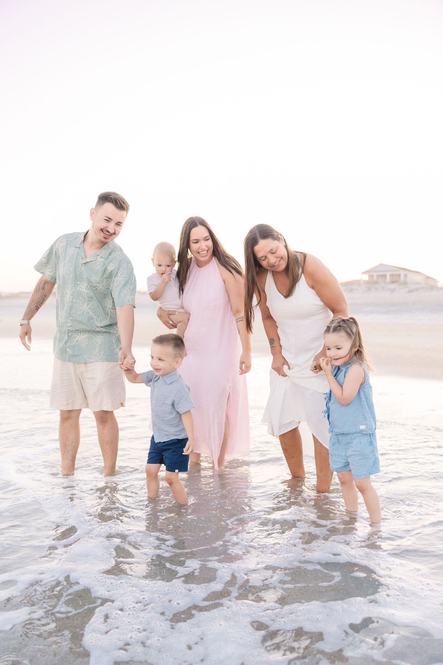 Family of six enjoying a sunny beach day, with parents and children playing in the ocean waves together.