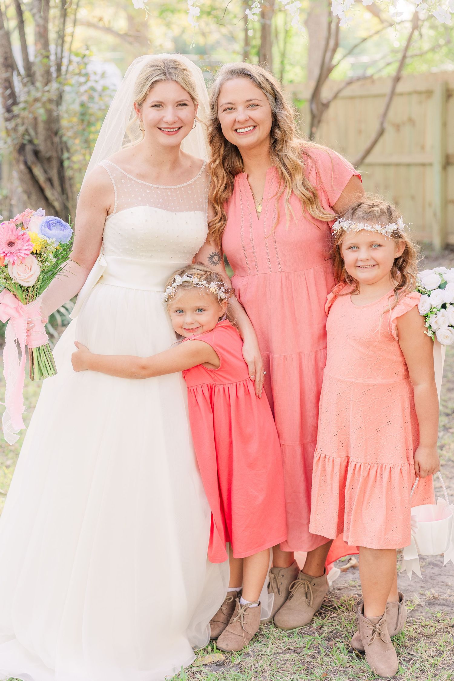 Bridesmaids in coral pink dresses stand together with bouquets at an outdoor wedding celebration wedding groom bride wilmington photographer