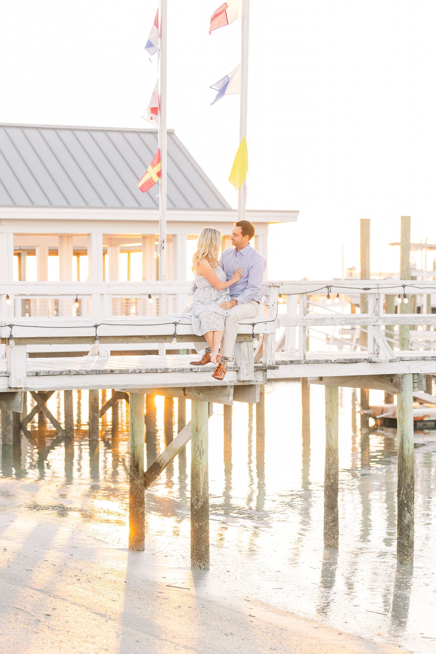 Dreamy waterfront engagement photo with couple on pier during golden hour.