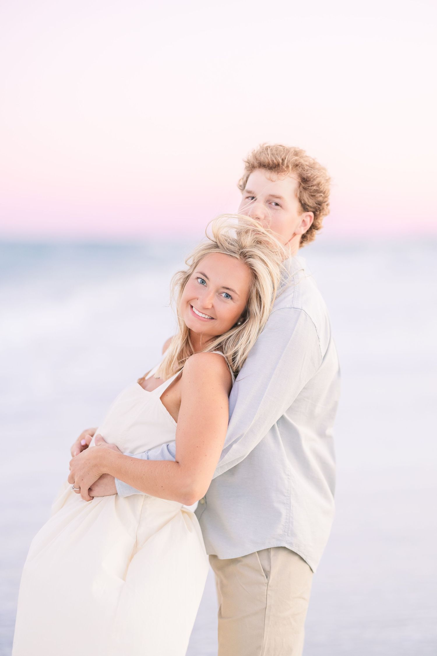 Romantic beach photoshoot with couple embracing in soft pastel lighting.
