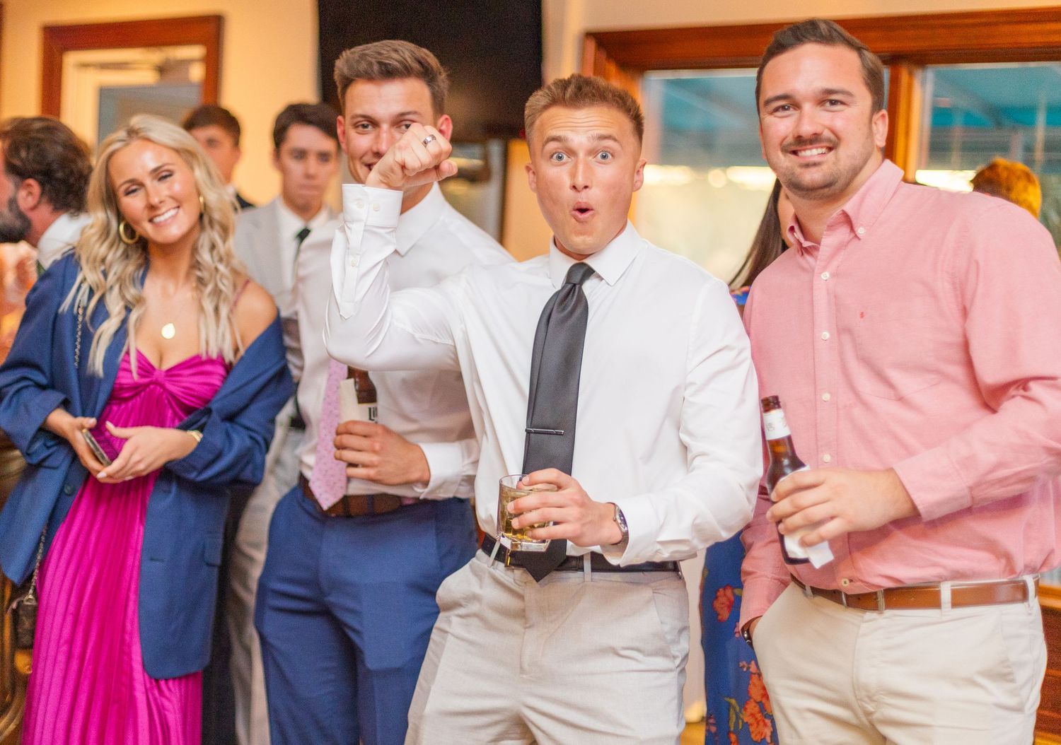 Wedding guests pose playfully with drinks at a reception, making silly expressions.