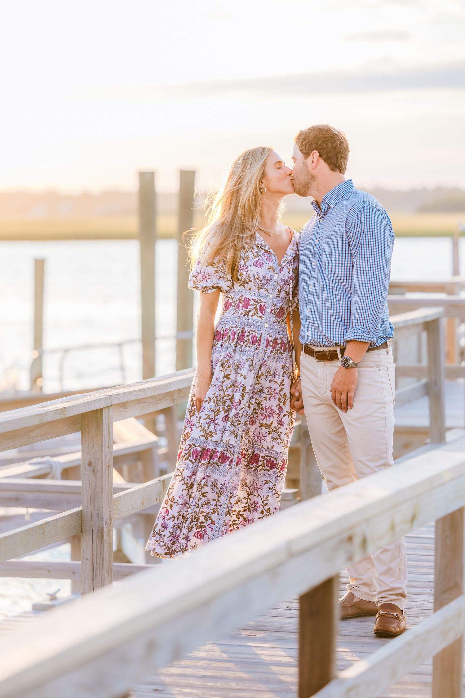 Romantic couple sharing intimate moments on a sunlit wooden boardwalk by the water.