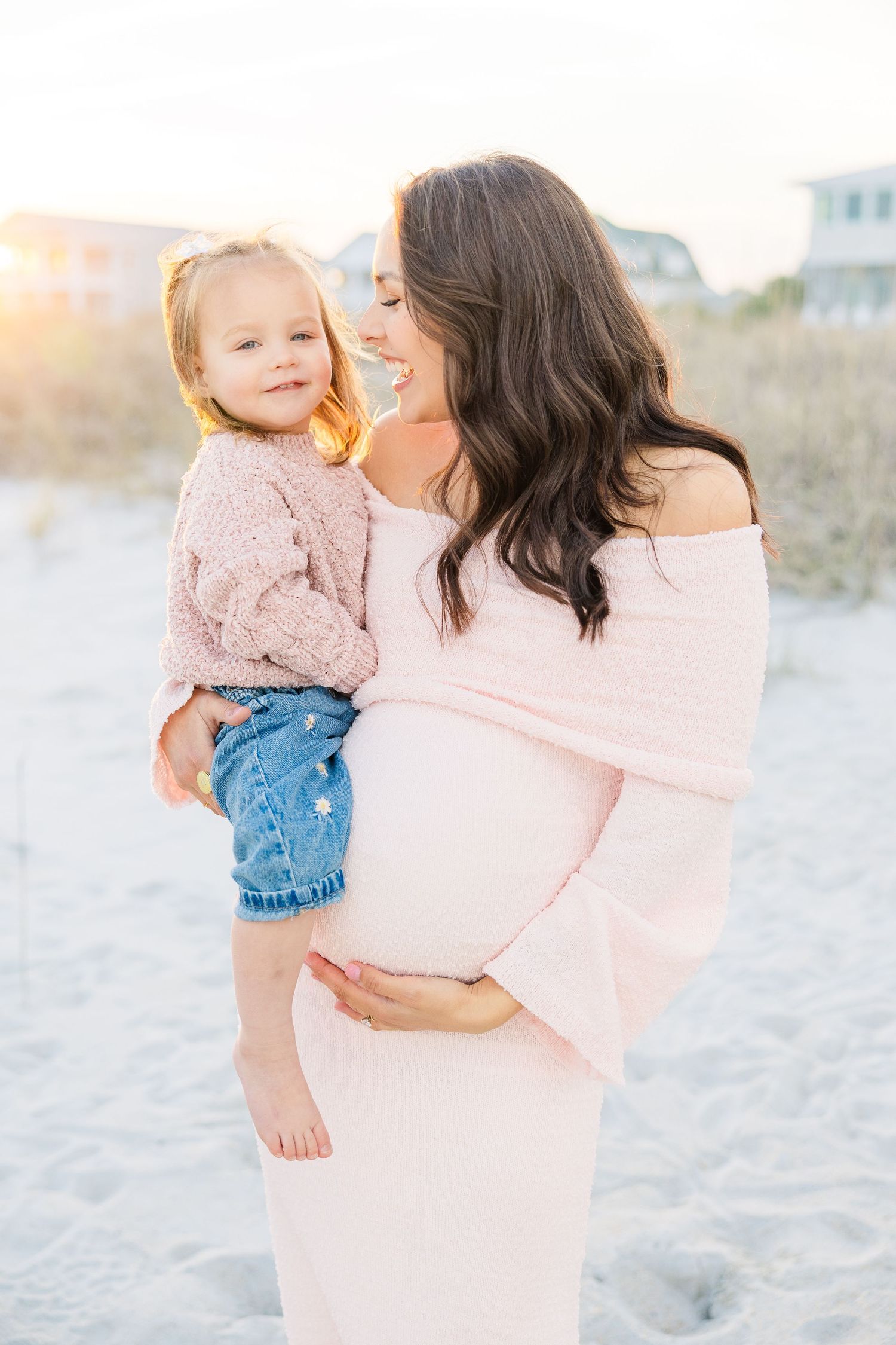 A tender beach photoshoot featuring soft pink and blue outfits against a sandy backdrop at sunset.