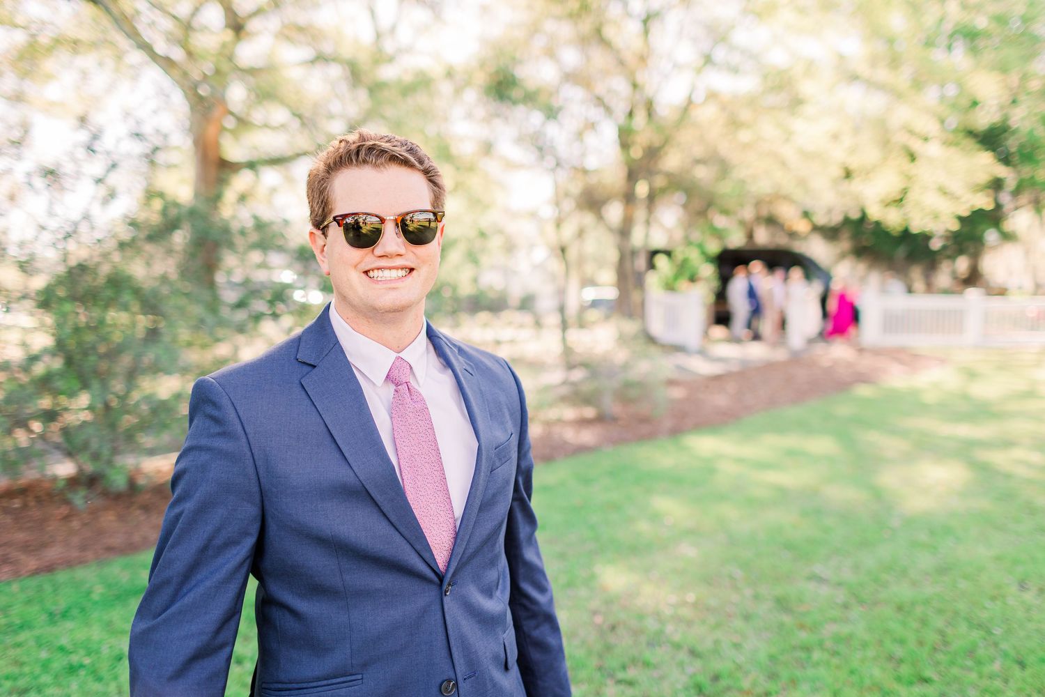 Groomsmen in navy suits and pink ties posing for formal wedding photos outdoors.