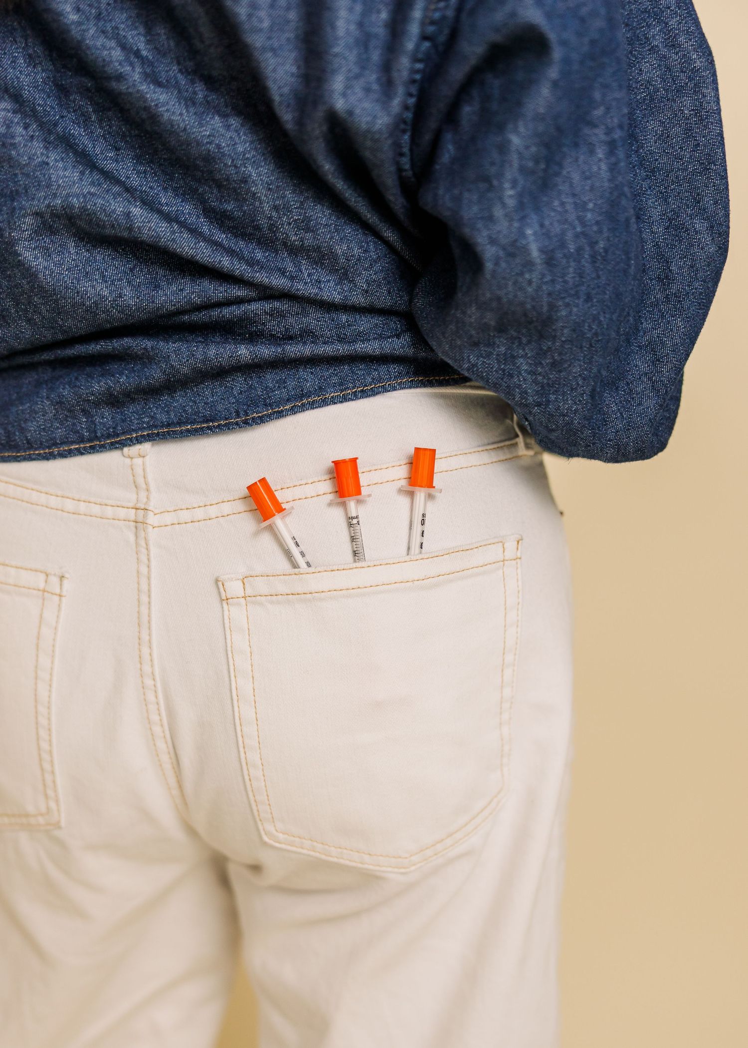 Close-up detail of denim shirt and white jeans with orange accents.